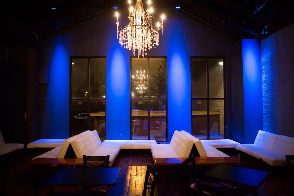 Chic interior with blue-lit walls, white cushioned seating, and a chandelier at Twenty Seven Venue in Little Rock Arkansas