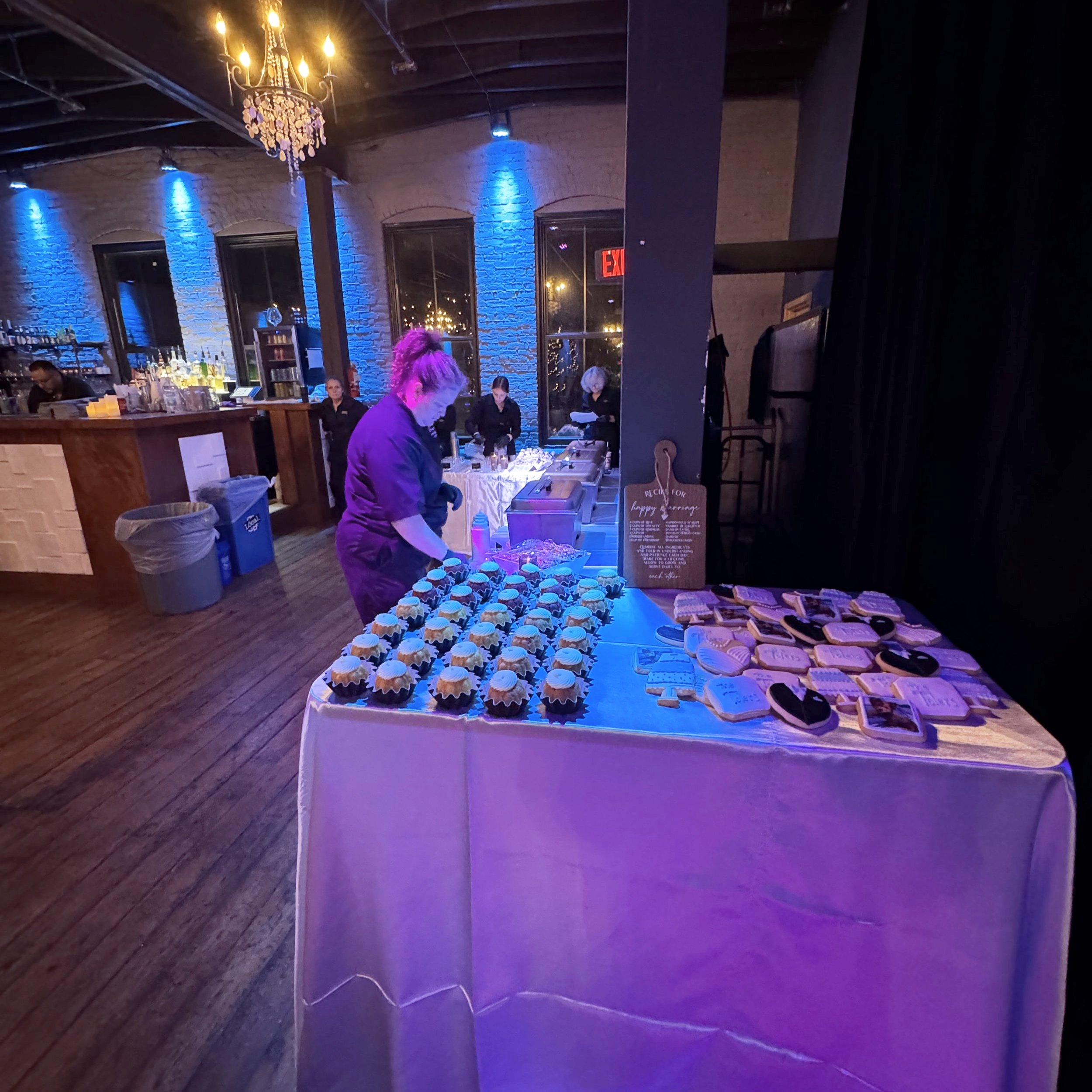 Twenty Seven event space in downtown Little Rock with purple lighting, a table with cupcakes and heart-shaped cookies, people working behind the table, and a bar area in the background.