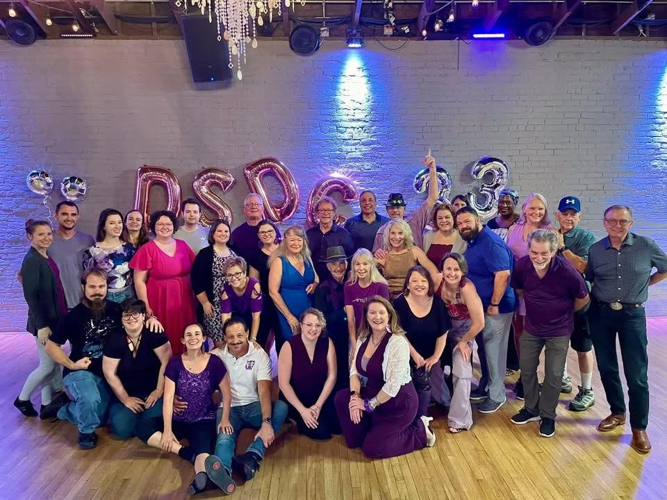 Group of people gathered at a celebration event at Twenty Seven Event Venue in downtown Little Rock  with balloons spelling "DSDC 13" in the background.
