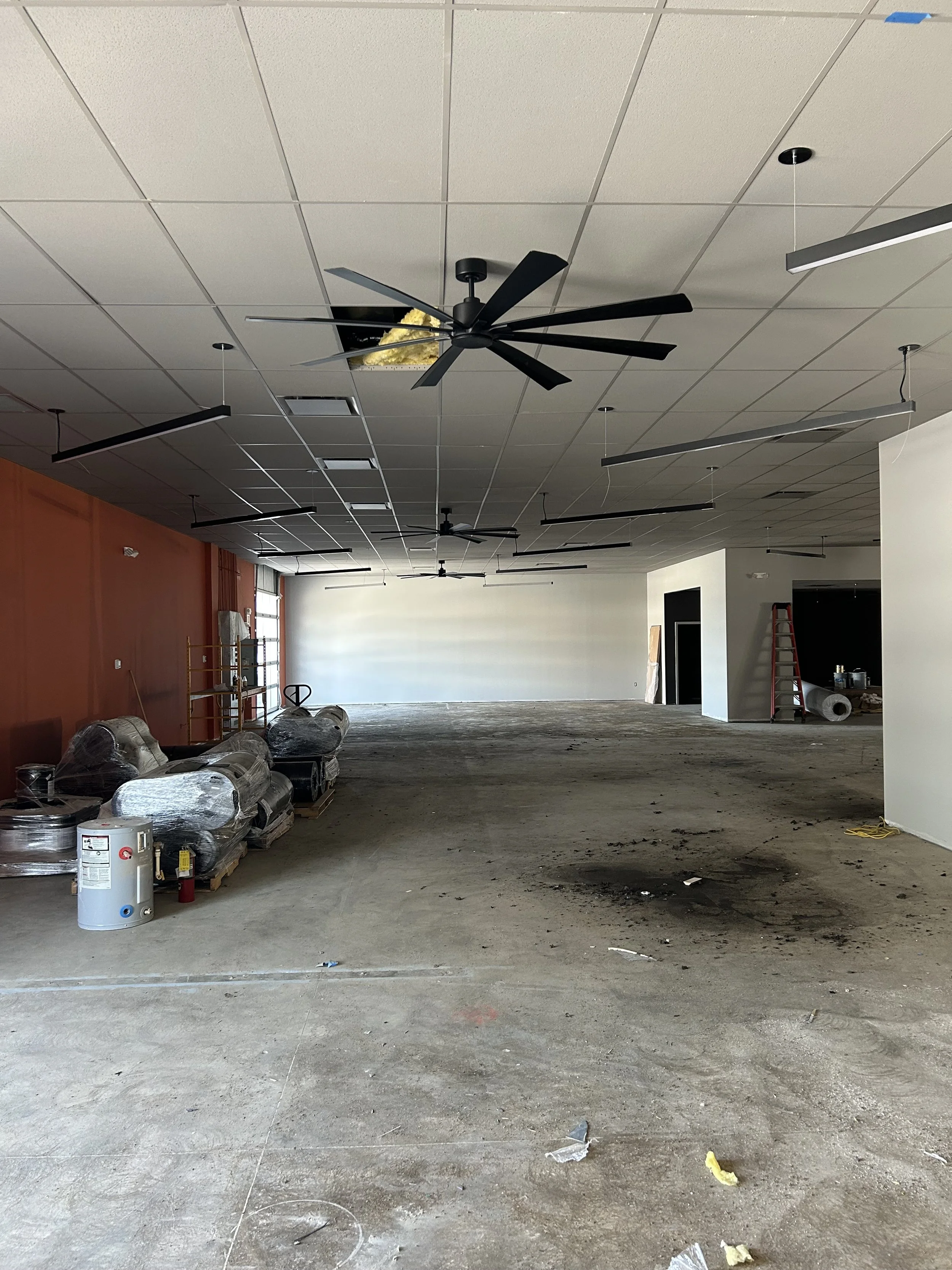 Open interior space at Crucible Fit during construction, with ceiling fans and unfinished flooring.