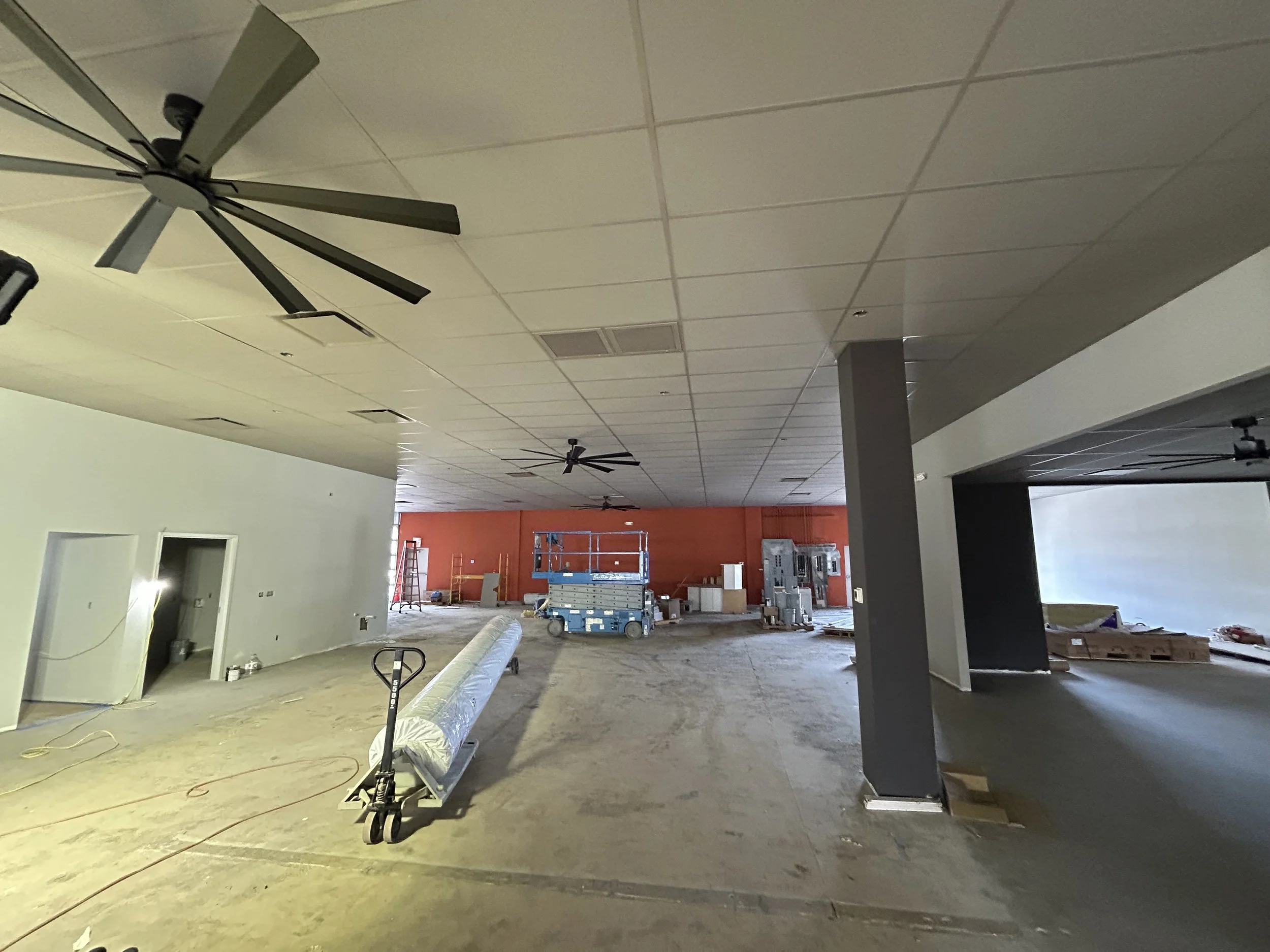 Crucible Fit construction progress showing an orange accent wall, exposed ductwork, and unfinished flooring.
