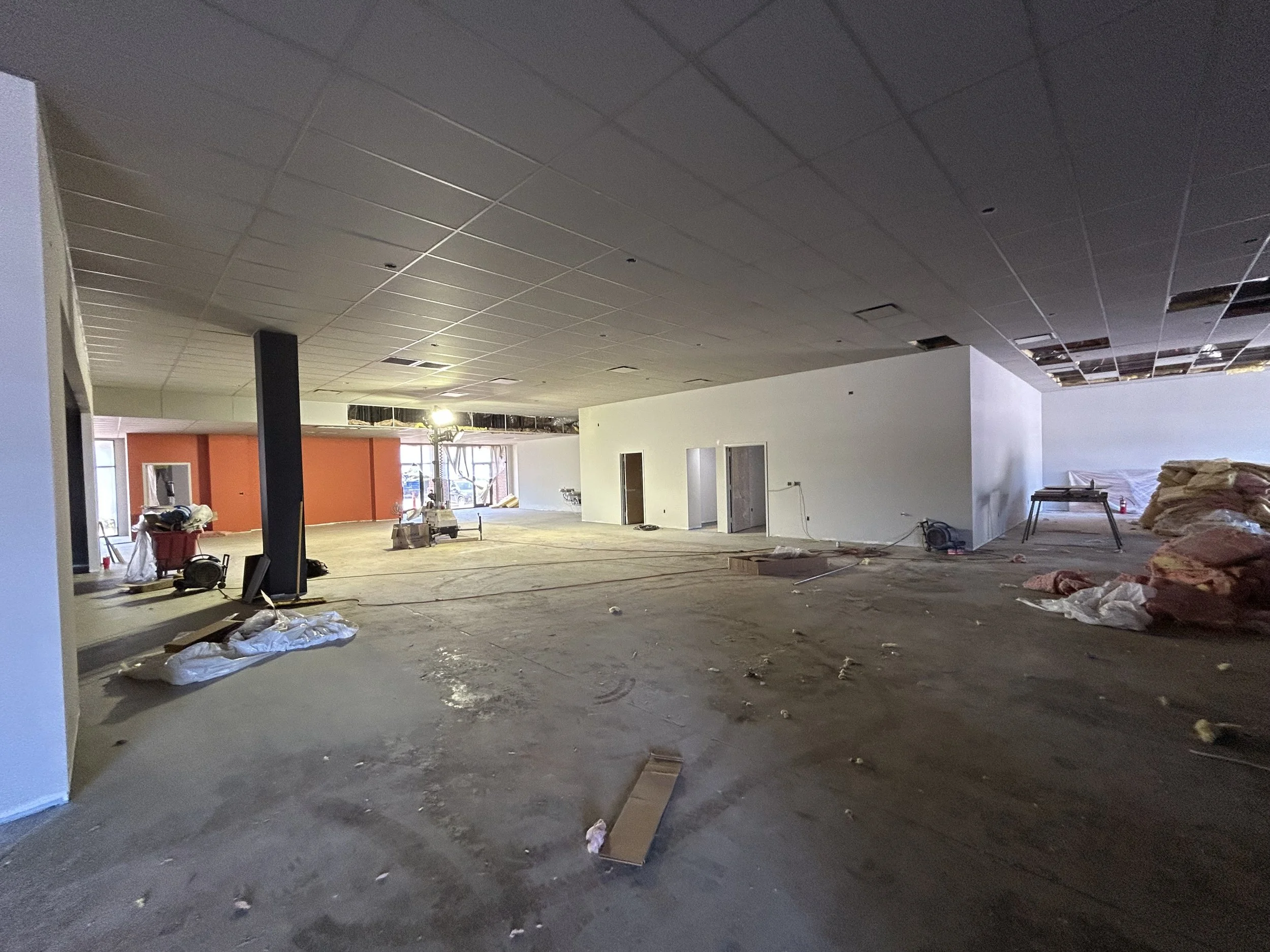 Crucible Fit gym buildout showing an orange accent wall, unfinished flooring, and ceiling installation in progress.
