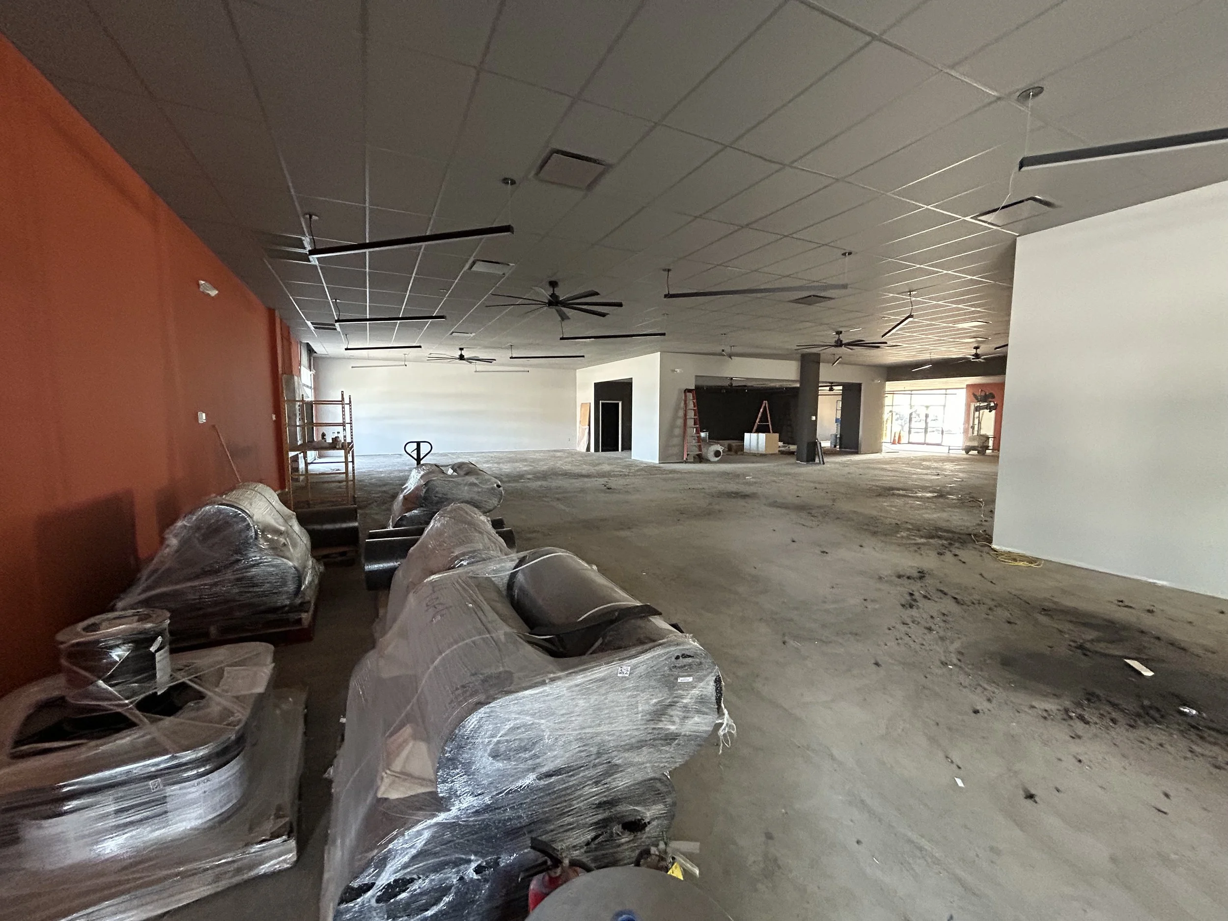 Crucible Fit interior under construction, with an orange accent wall, open floor space, and wrapped seating.