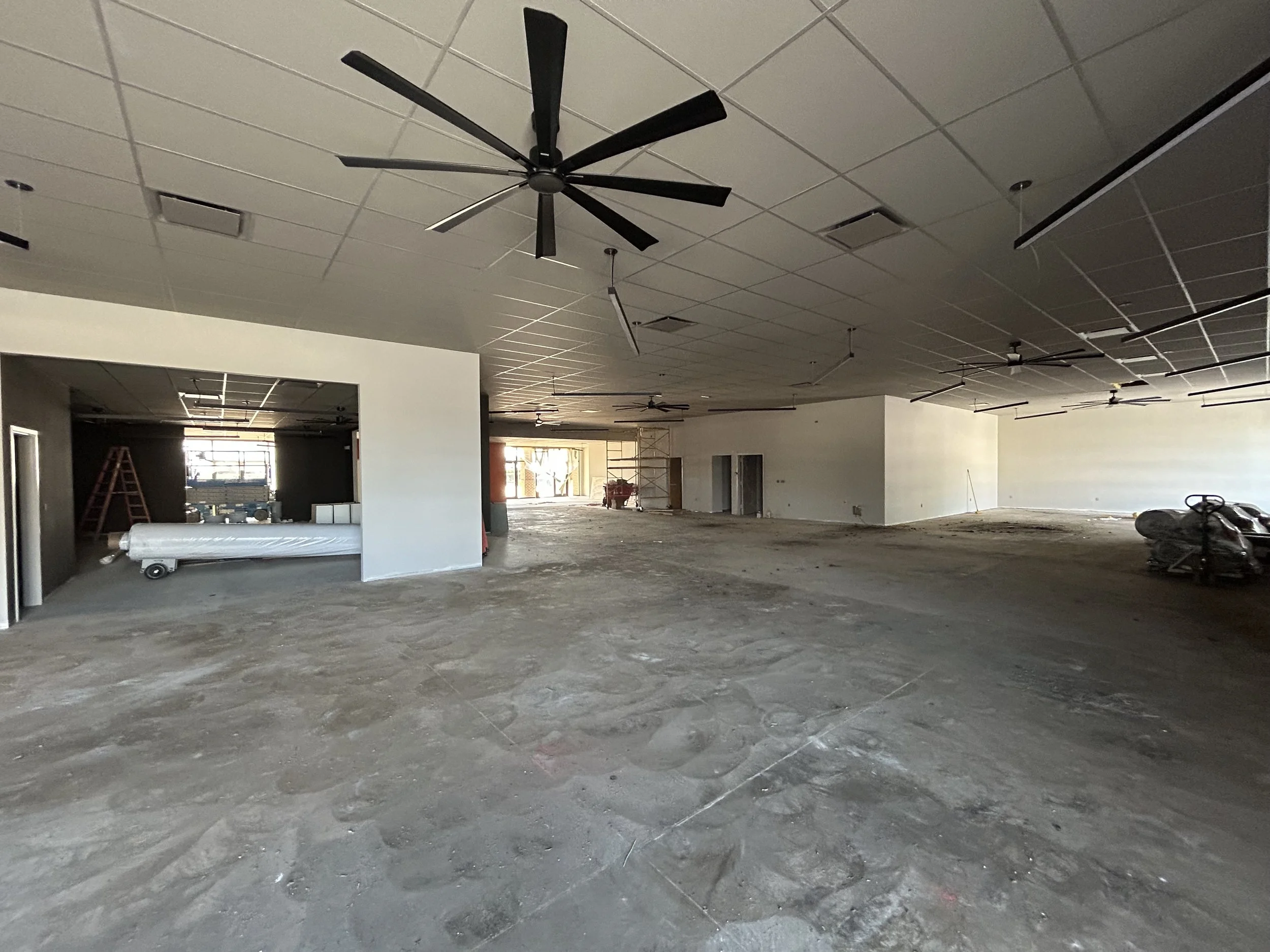 Crucible Fit interior under construction with black ceiling fans and unfinished flooring.