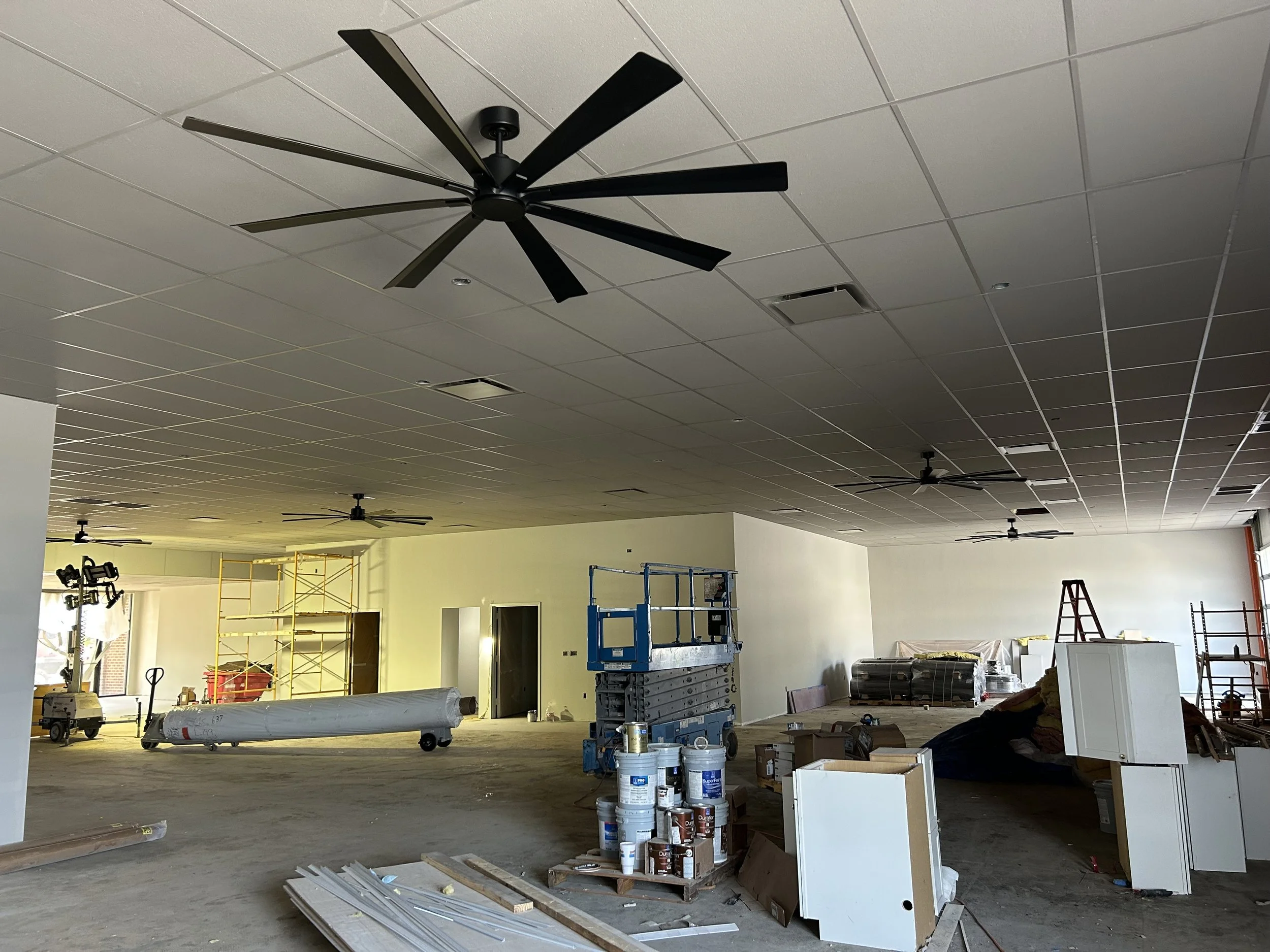 Crucible Fit gym construction progress with a large ceiling fan, unfinished walls, and materials awaiting installation.