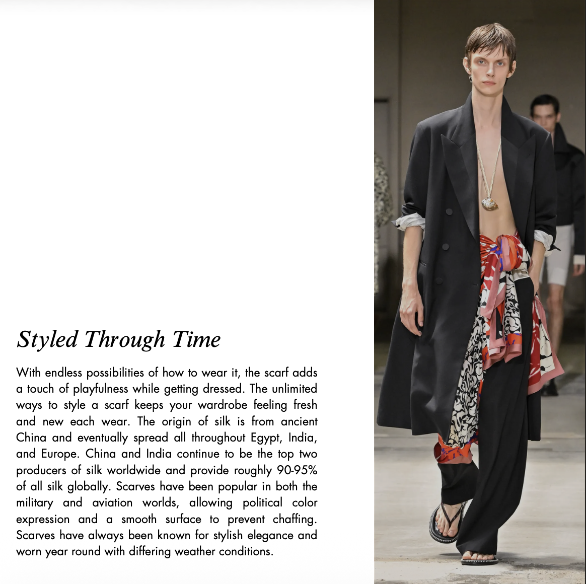 Fashion model wearing an oversized black blazer and trousers with a colorful silk scarf tied at the waist on a runway.
