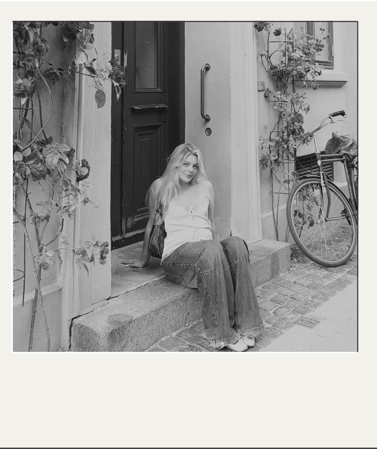 Woman sitting on a doorstep beside a vine-covered doorway and vintage bicycle