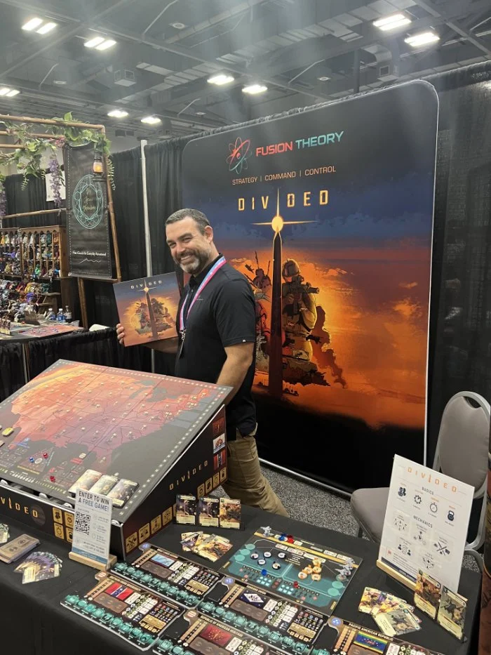 Joey Co-designer at the fusion theory booth holding the Divided gamebaord