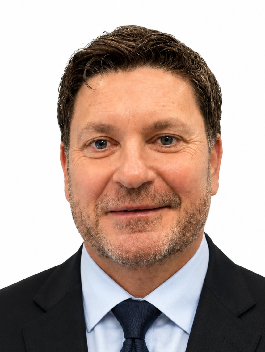 Headshot of a middle-aged man with brown hair and a beard, wearing a black suit, light blue shirt, and dark tie against a white background.