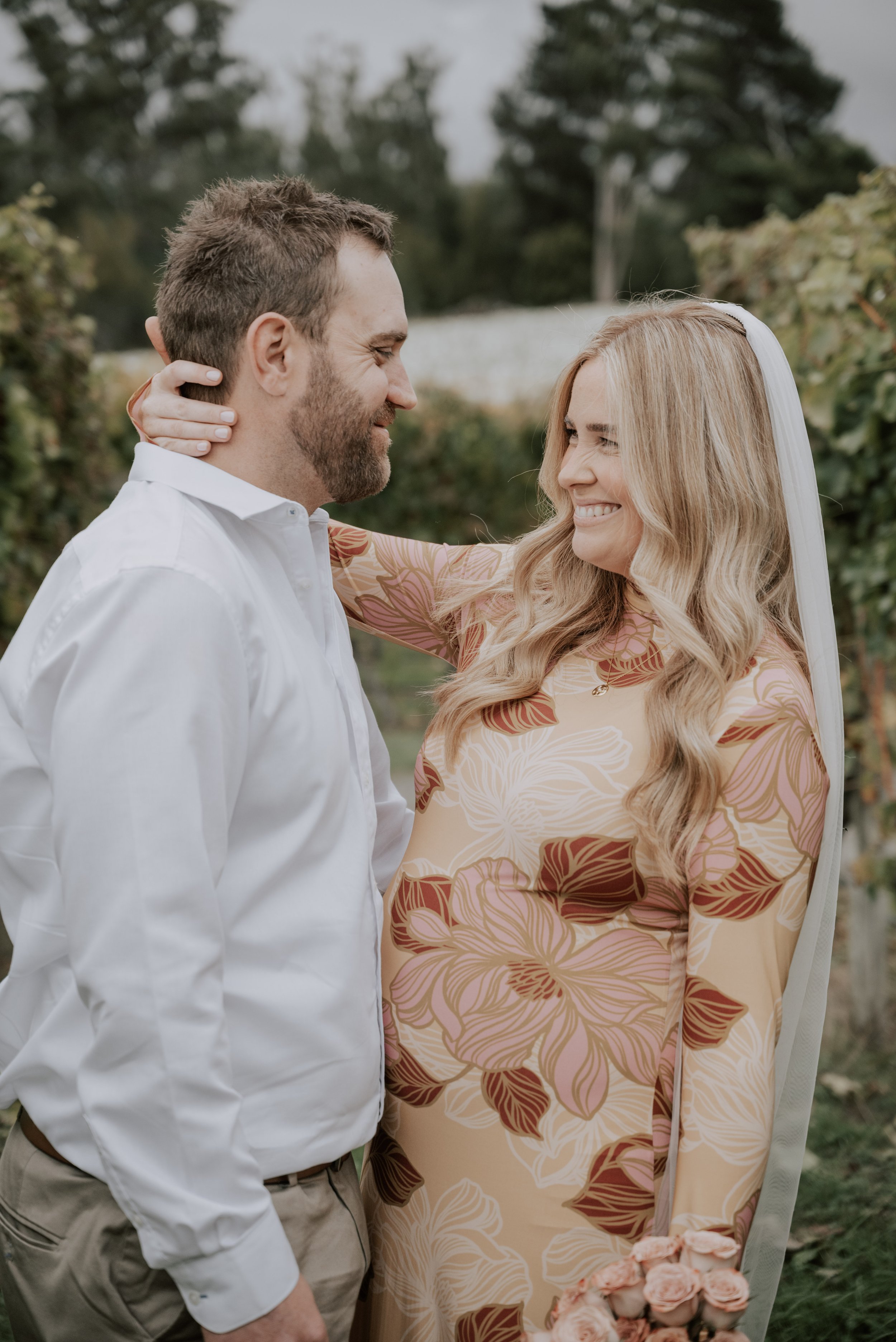 A bride and groom smiling at each other outdoors during their wedding ceremony or celebration.