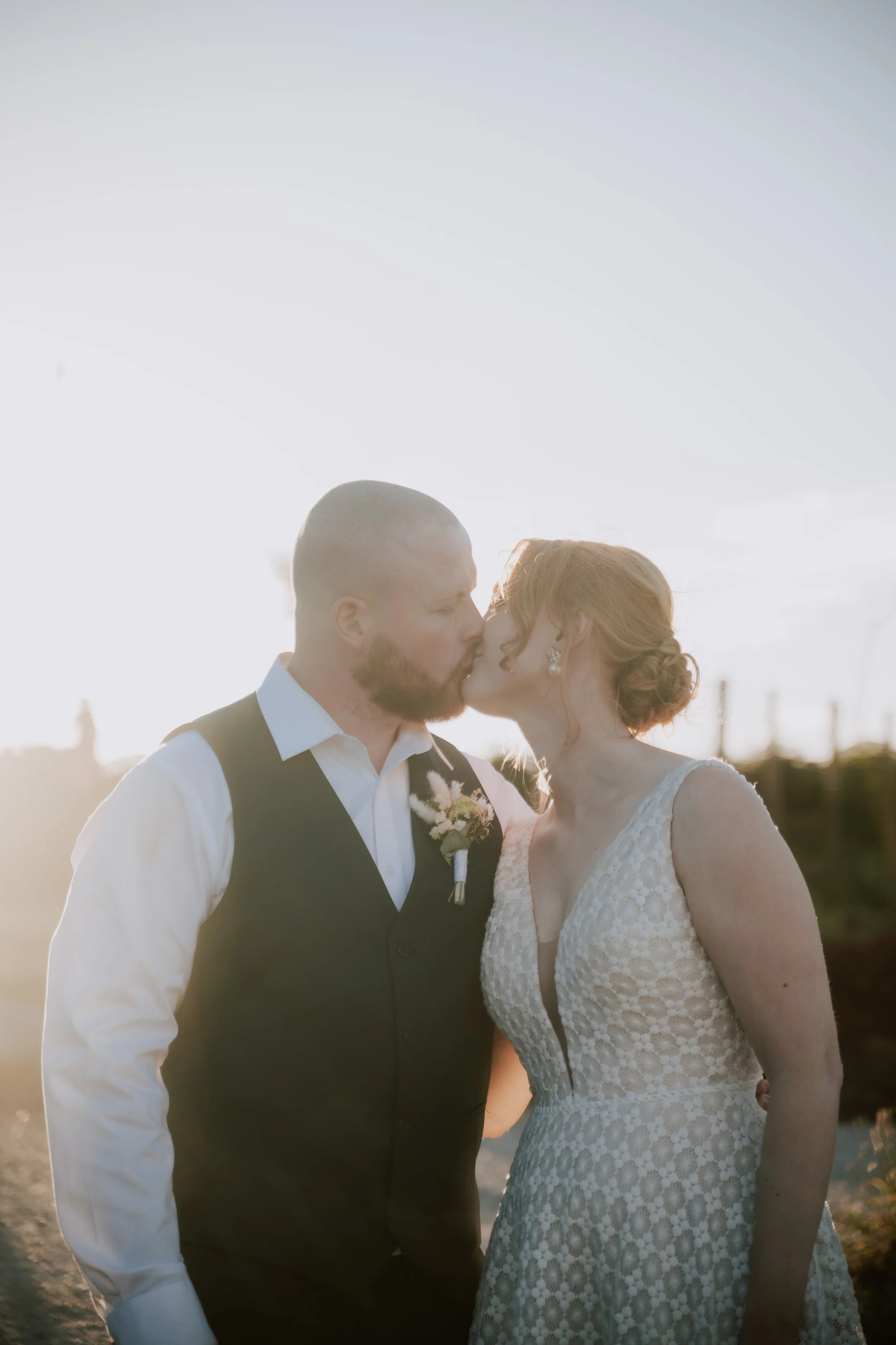 A couple in wedding attire sharing a kiss outdoors during golden hour.