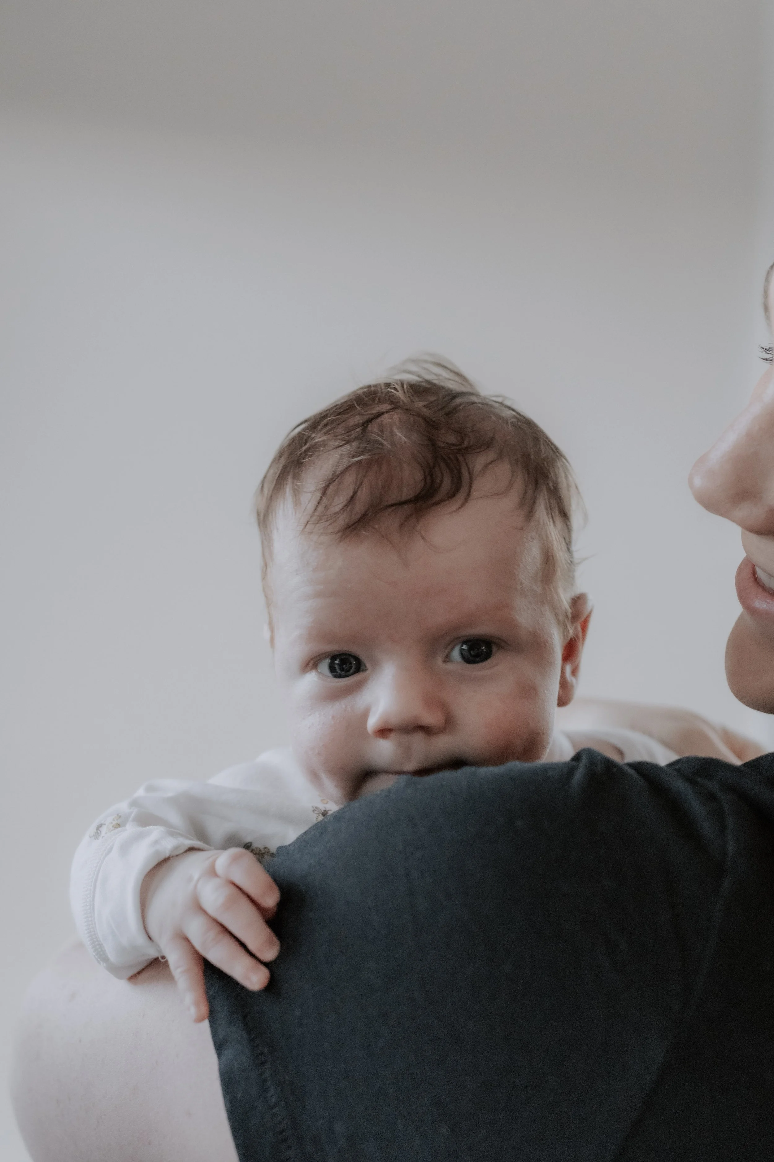 Baby looking at camera over the shoulder of his mother