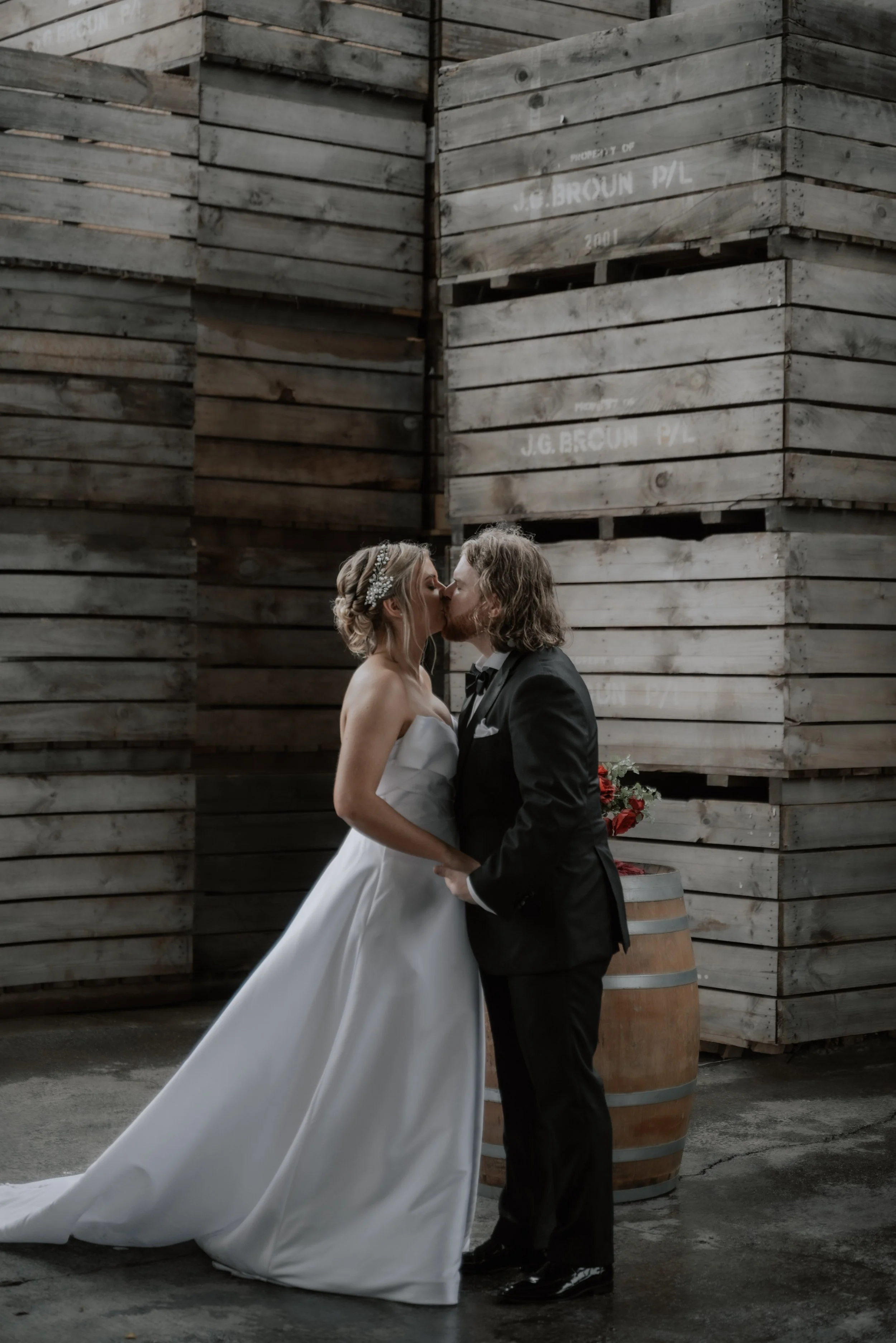 Couple kiss in front of apple crates during a wedding ceremony on a rainy day
