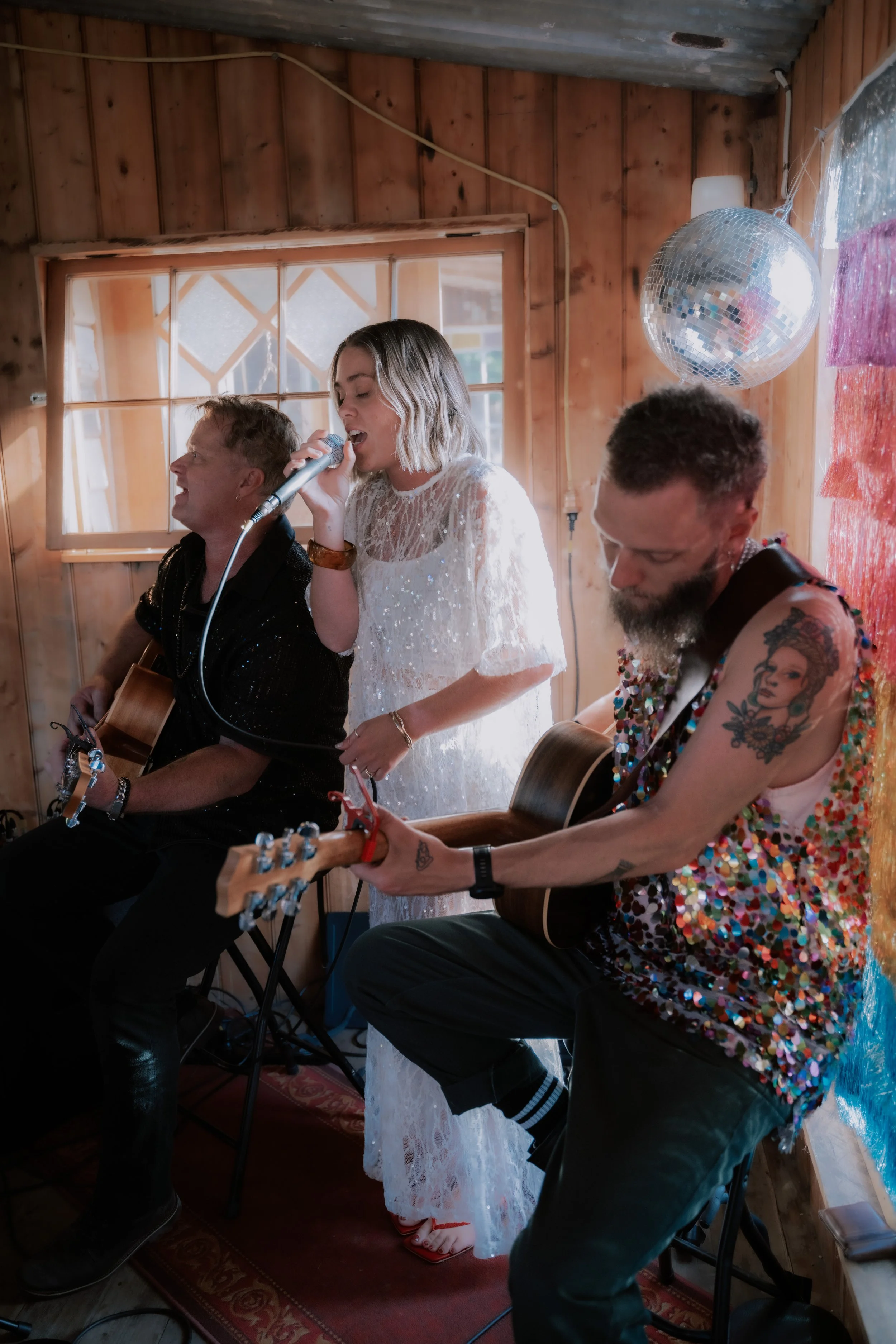 People singing and playing guitars in a wooden room, with a disco ball hanging from the ceiling.