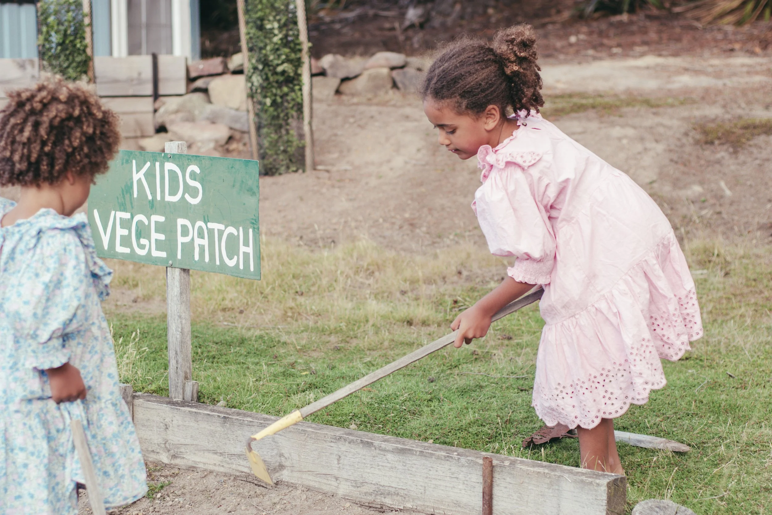 Two small children playing in a kids vege patch, in cute dresses