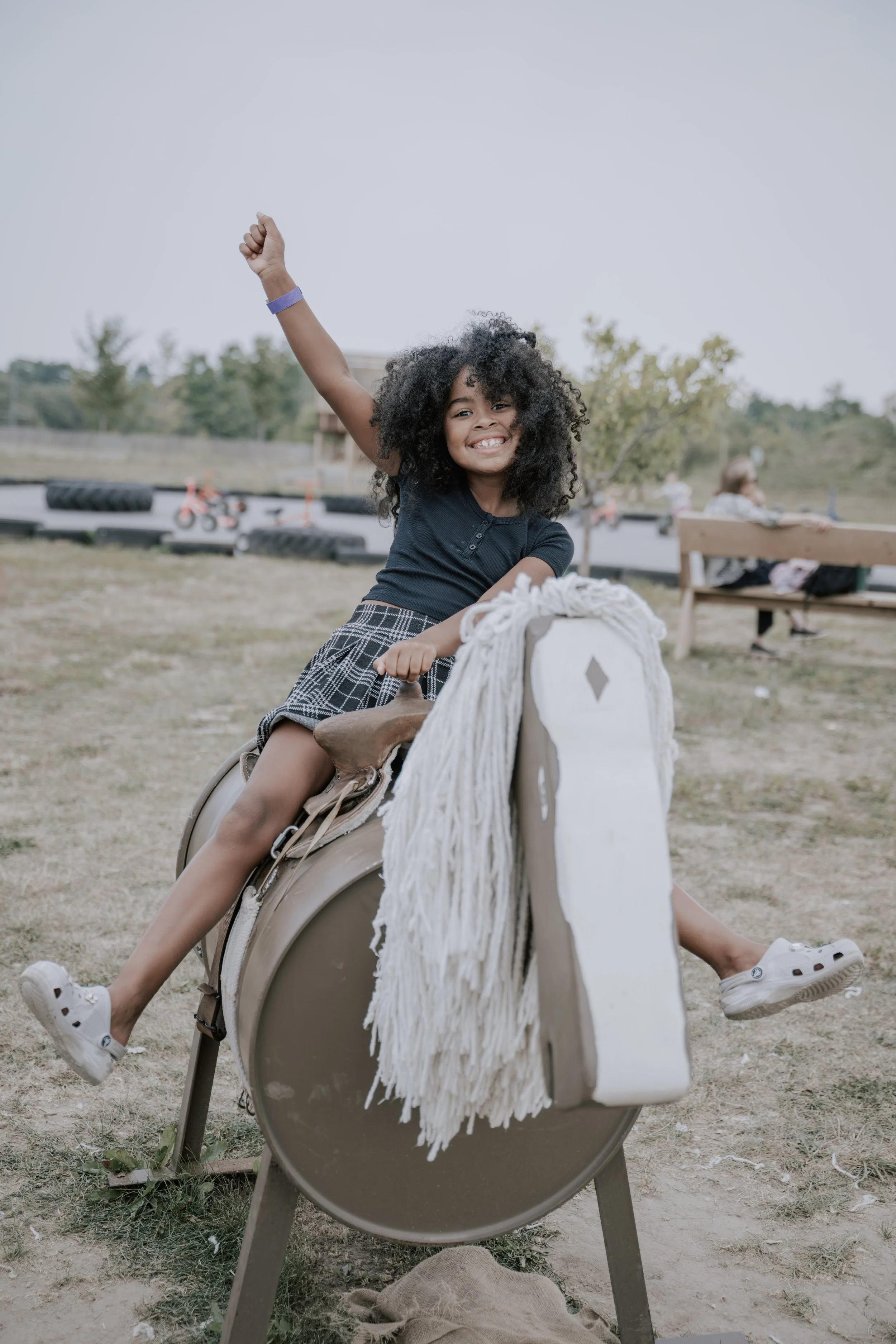 Happy girl riding a pretend horse at a playground while smiling and raising her arm
