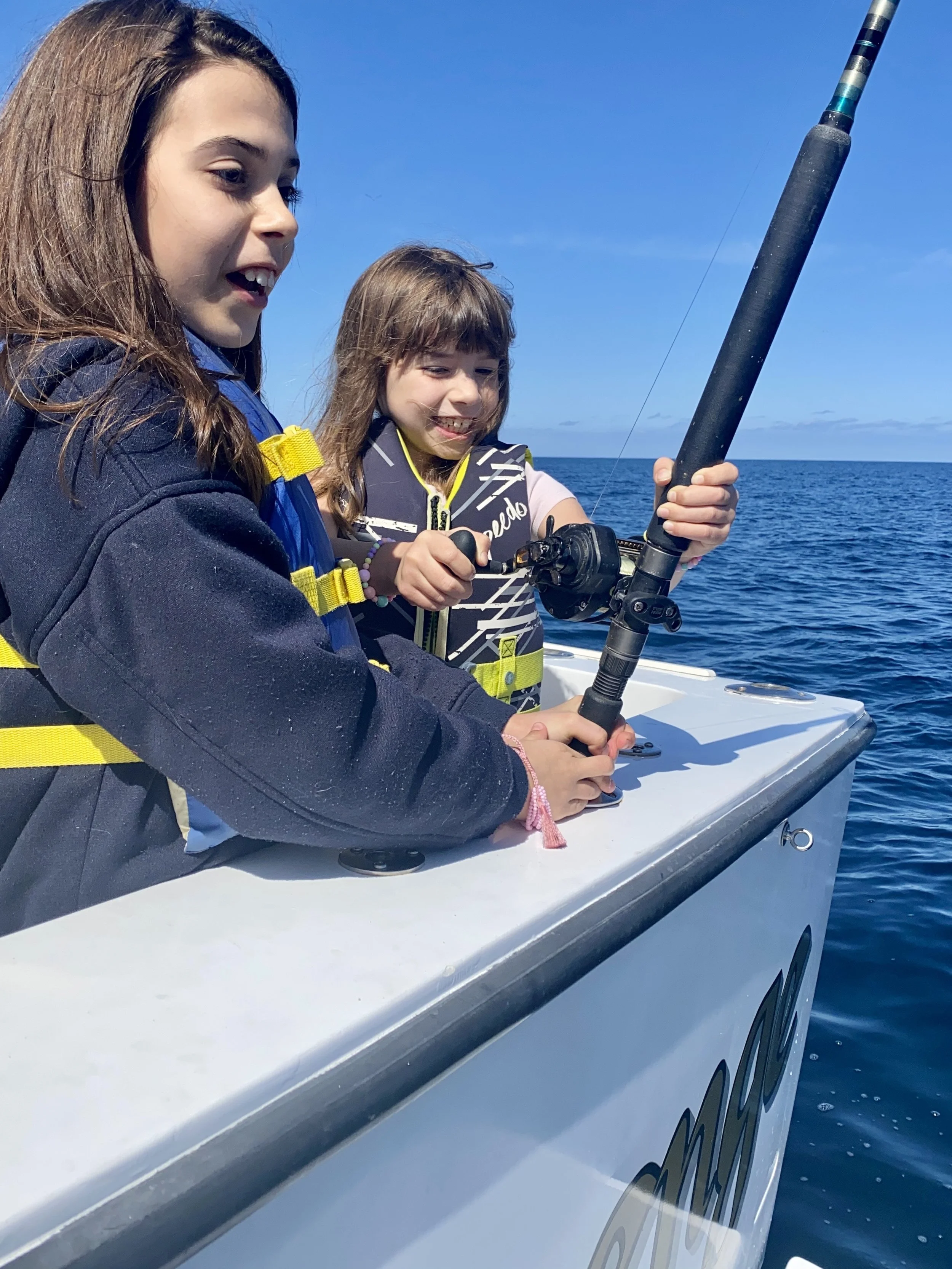 Two young girls fishing from a boat on the ocean on a sunny day.