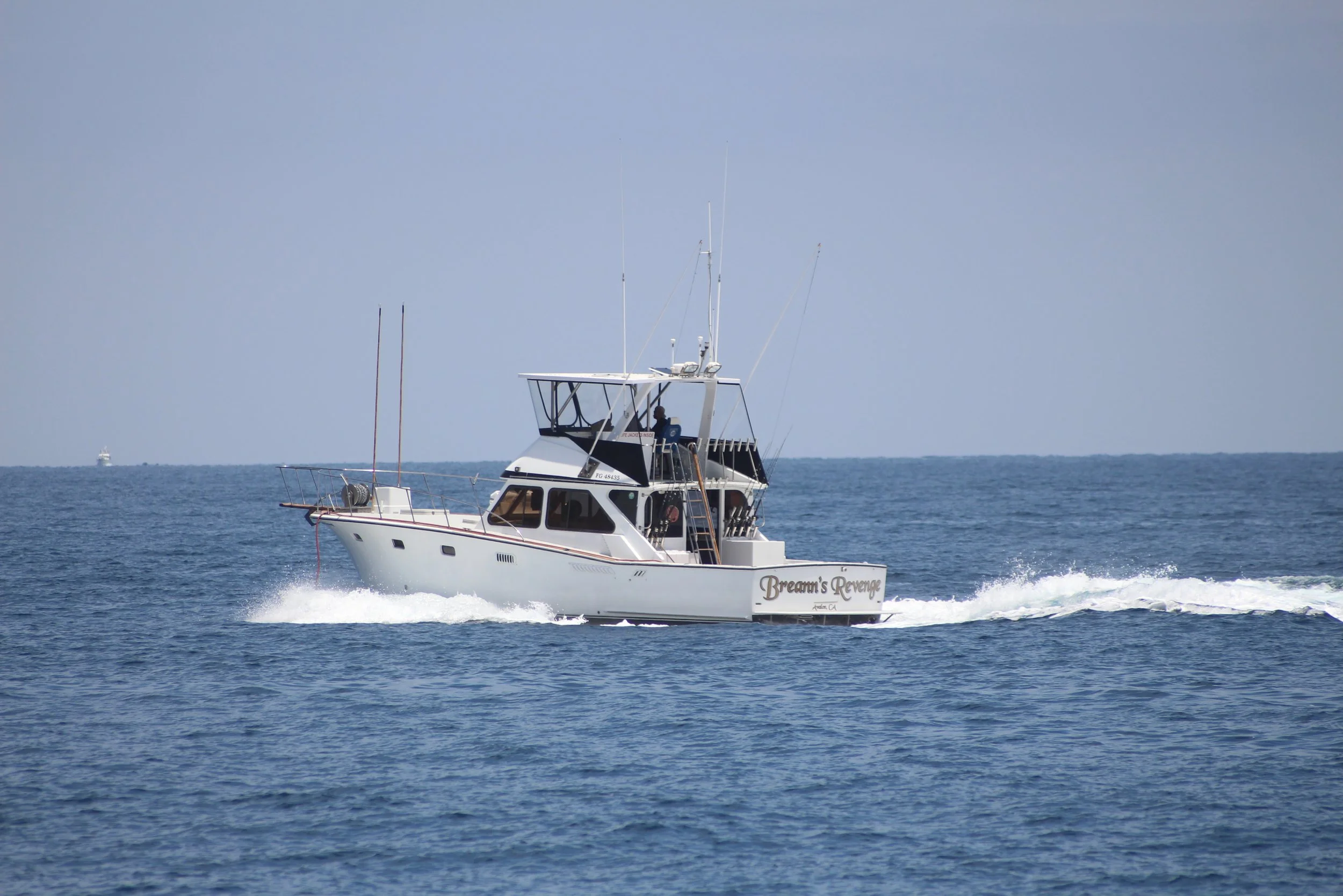 A white motorboat named 'Dream's Revenge' sailing on the ocean with a wake behind it, under a blue sky.