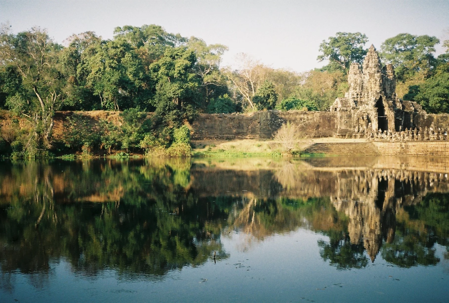 Ancient stone temple surrounded by lush green trees, reflected in calm water.