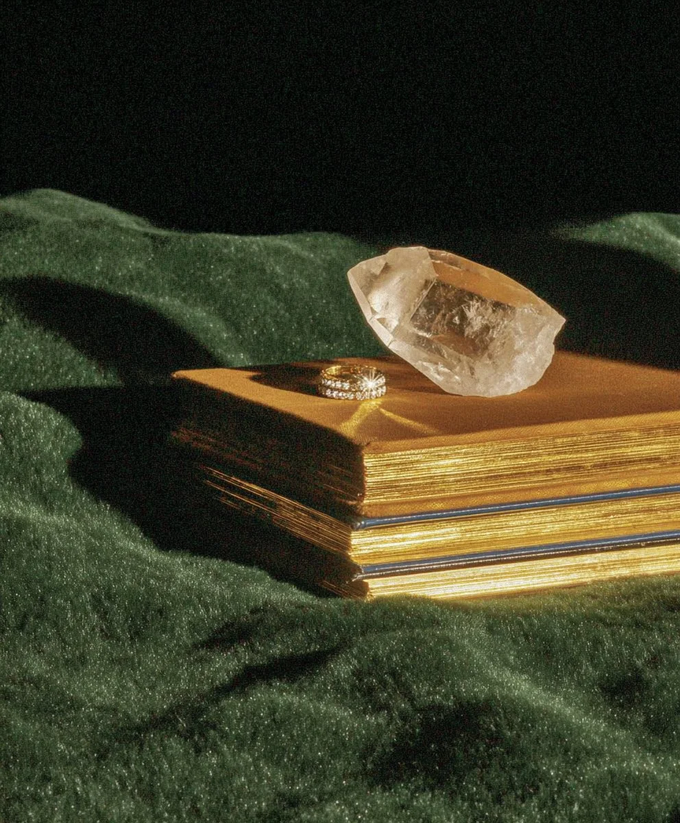 A gold stack of three books with a ring and a large rough gemstone on top, all placed on dark green velvet fabric.