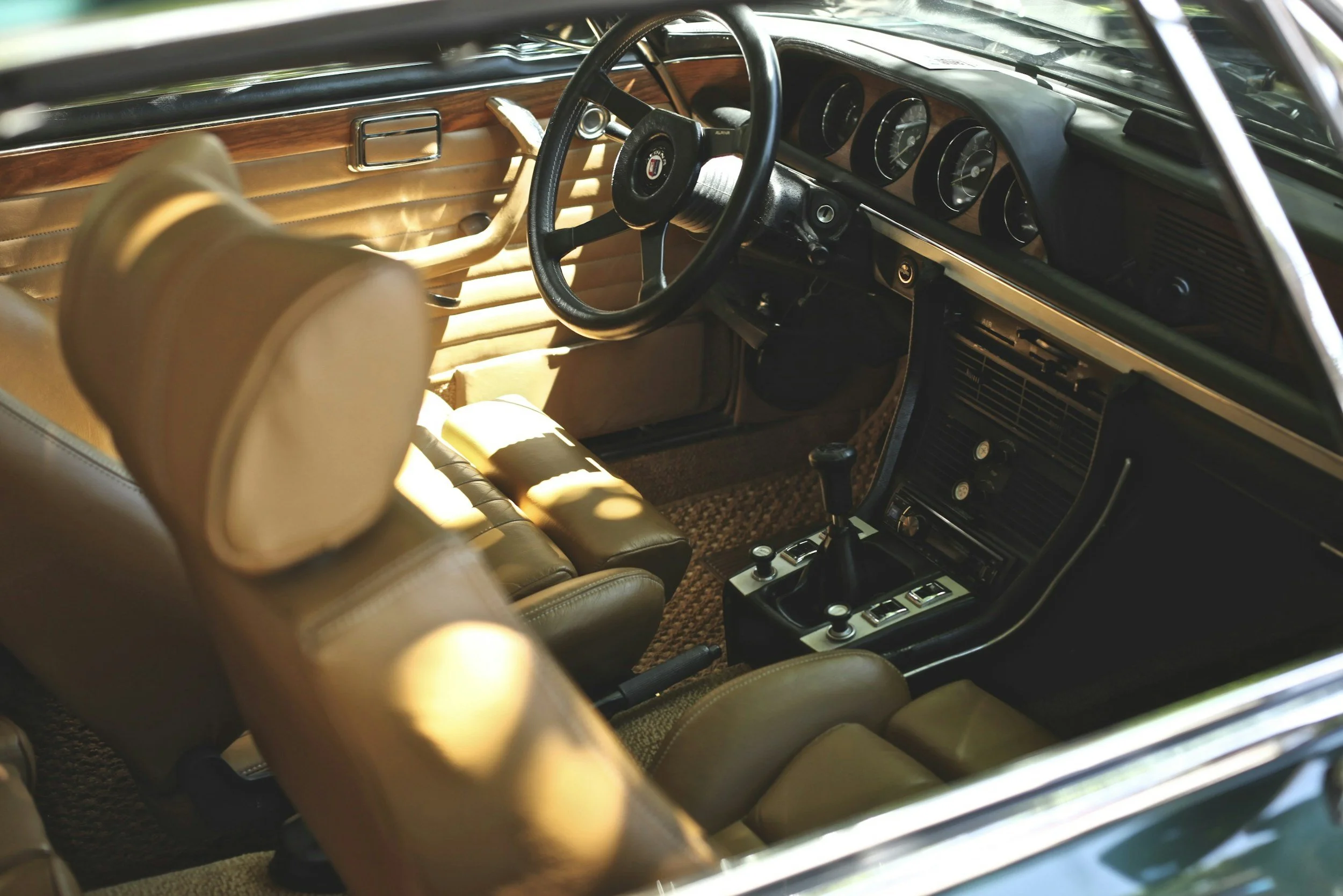 Interior of a vintage car with tan leather seats, a black steering wheel, and classic dashboard gauges.