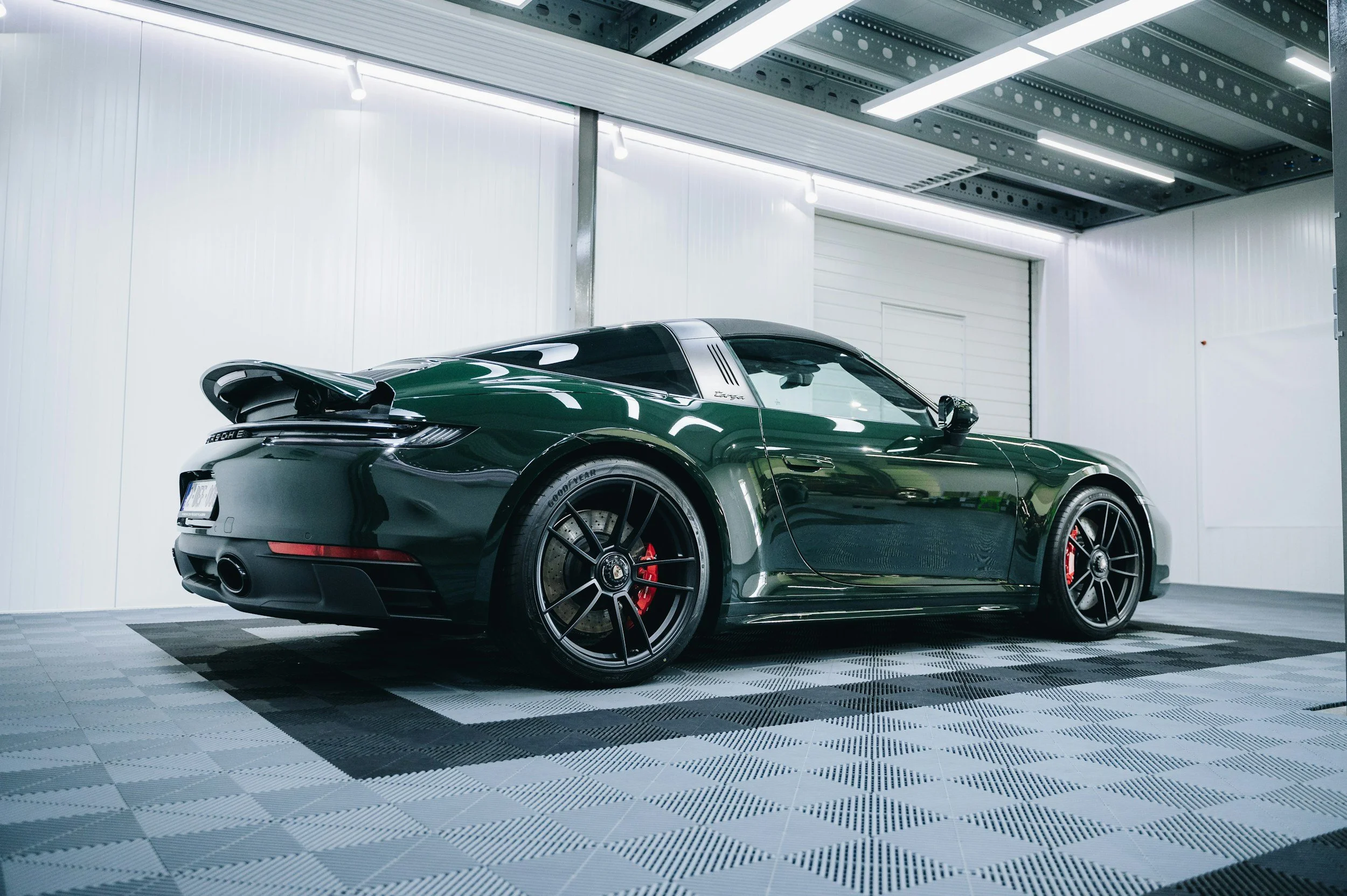 Black sports car with red brake calipers parked on a checkered floor inside a well-lit garage.