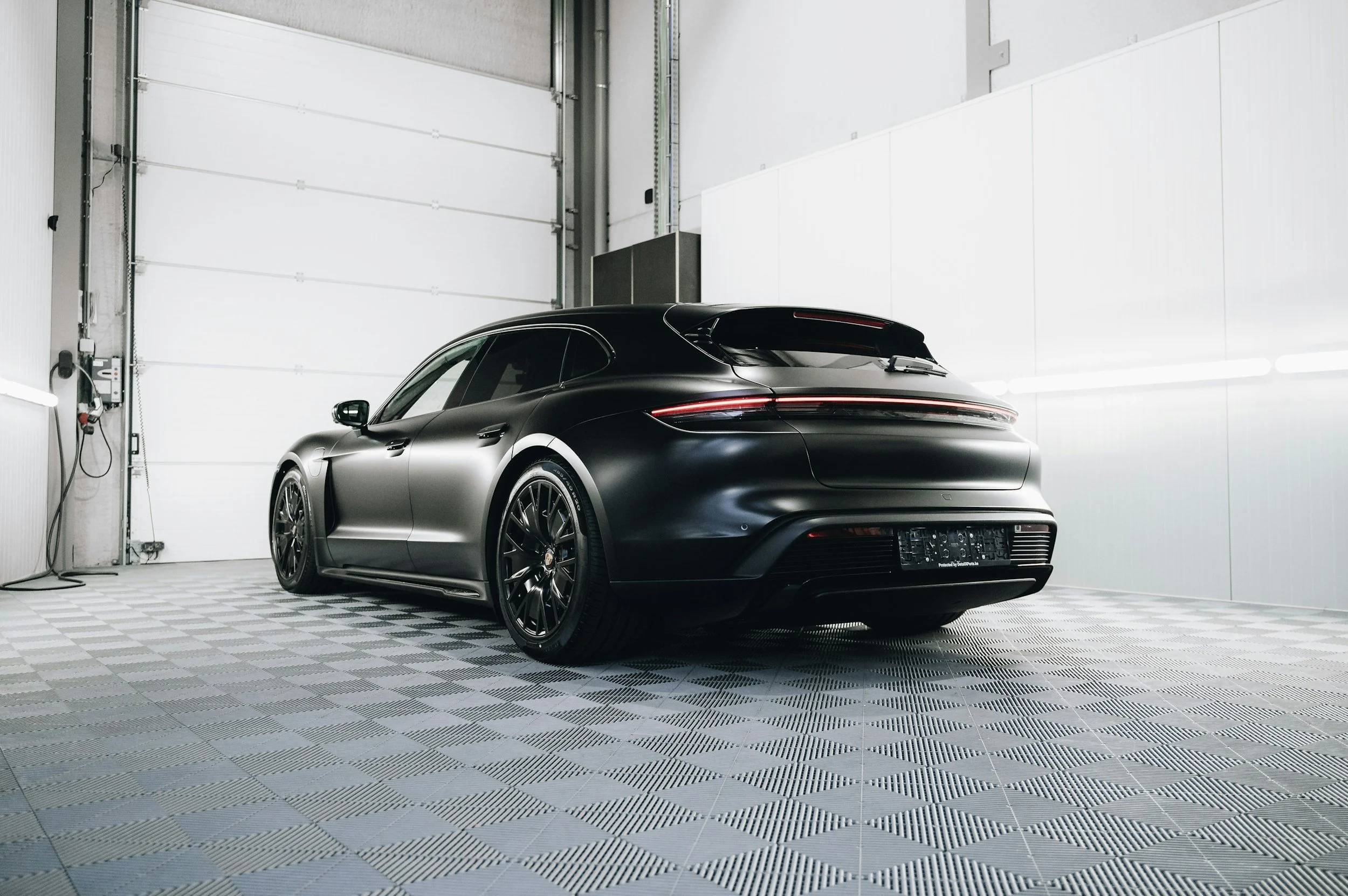 A sleek black luxury car parked inside a well-lit garage with a checkered floor.