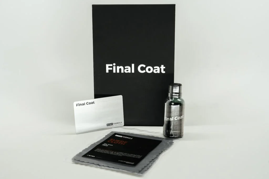 A car detailing kit includes a black box labeled 'Final Coat', a small bottle of cleaning solution, a packet of detailing wipes, and a white card, all arranged neatly against a plain white background.