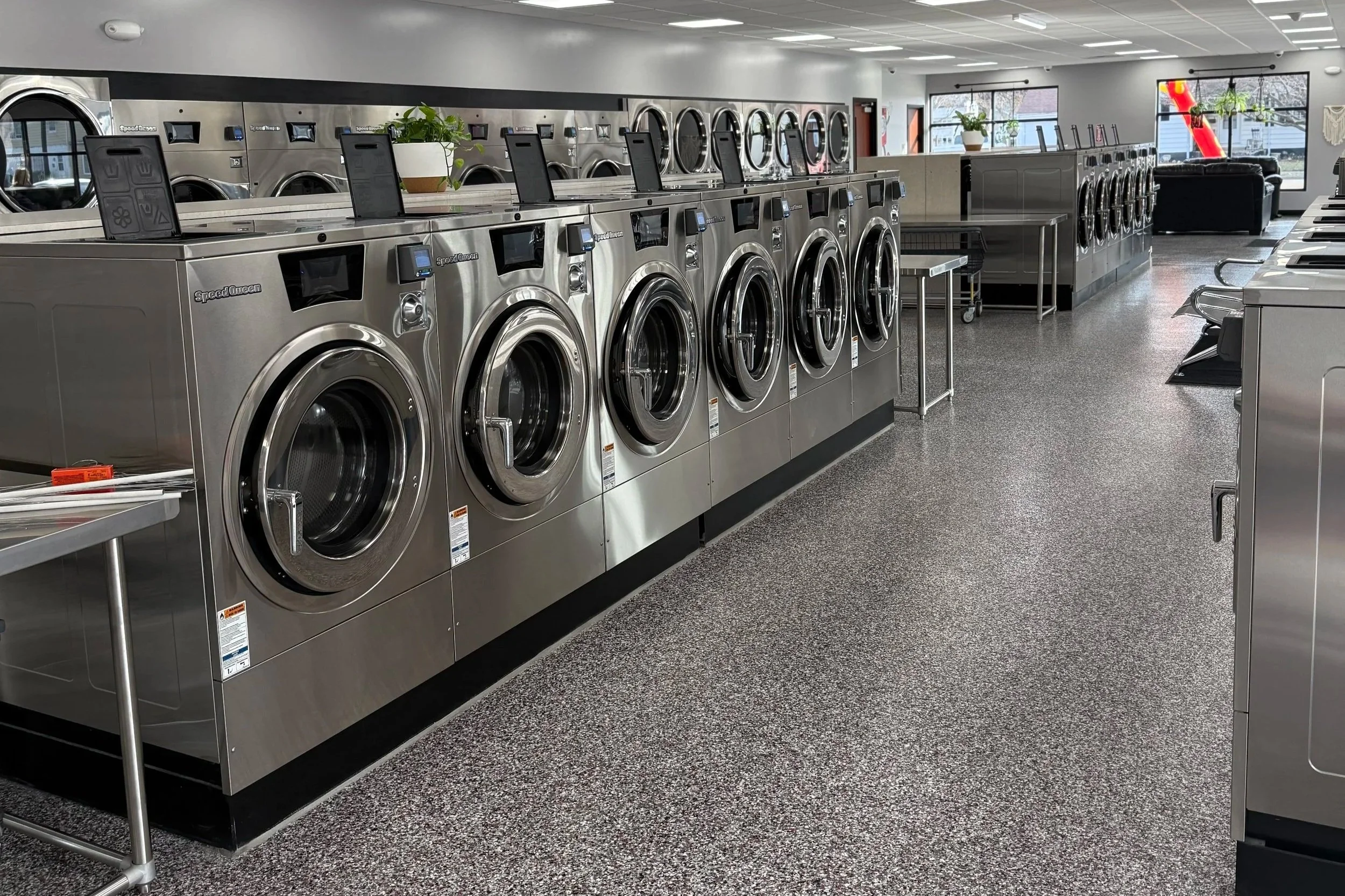 Laundry room with multiple front-loading washing machines and dryers, some with digital screens, and a table with laundry supplies in a laundromat.