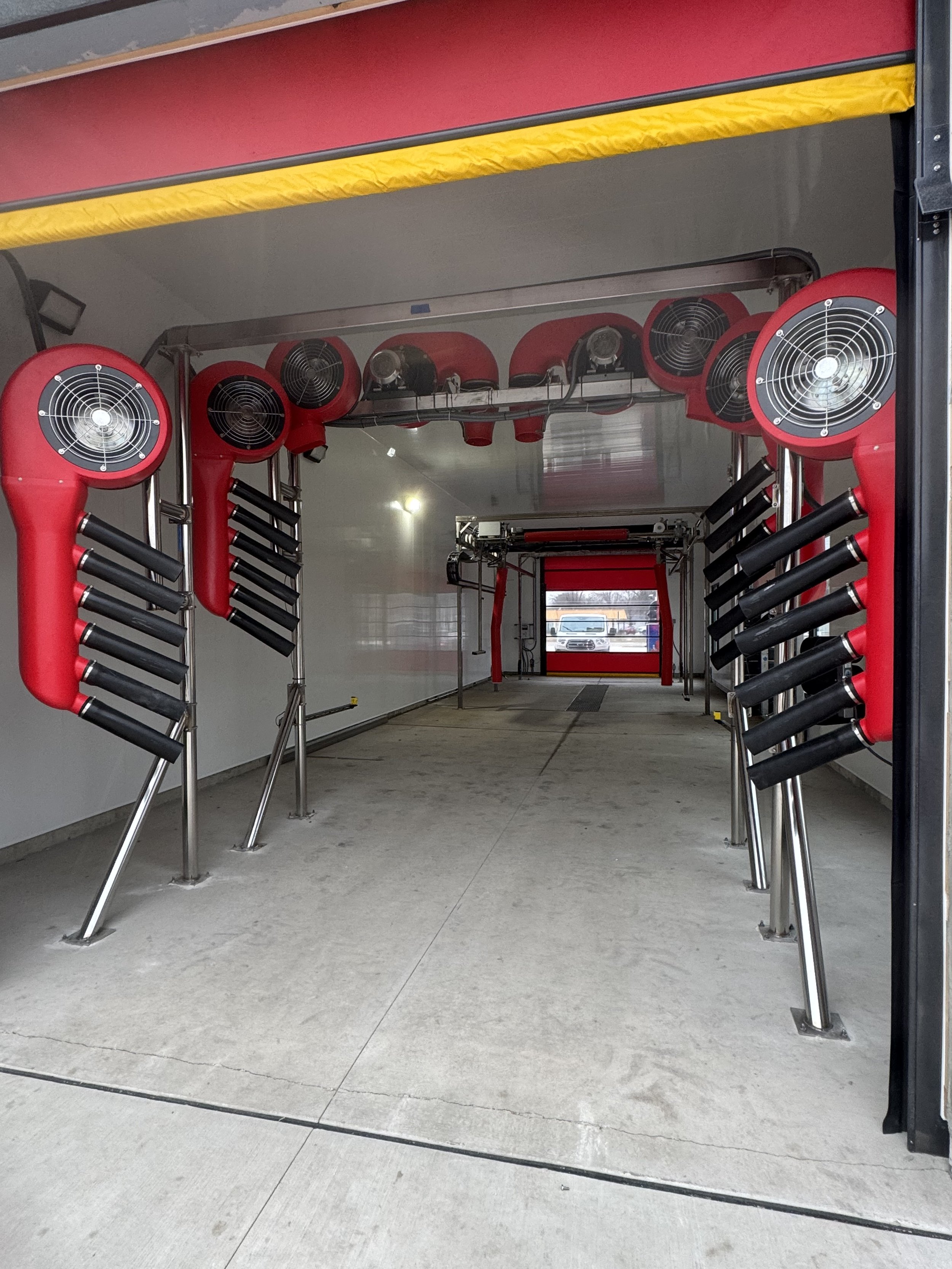 Inside view of a mobile ice rink trailer, showing red fans and drum rotors along the sides and ceiling, with a clear path to the back where a window displays parked cars outside.