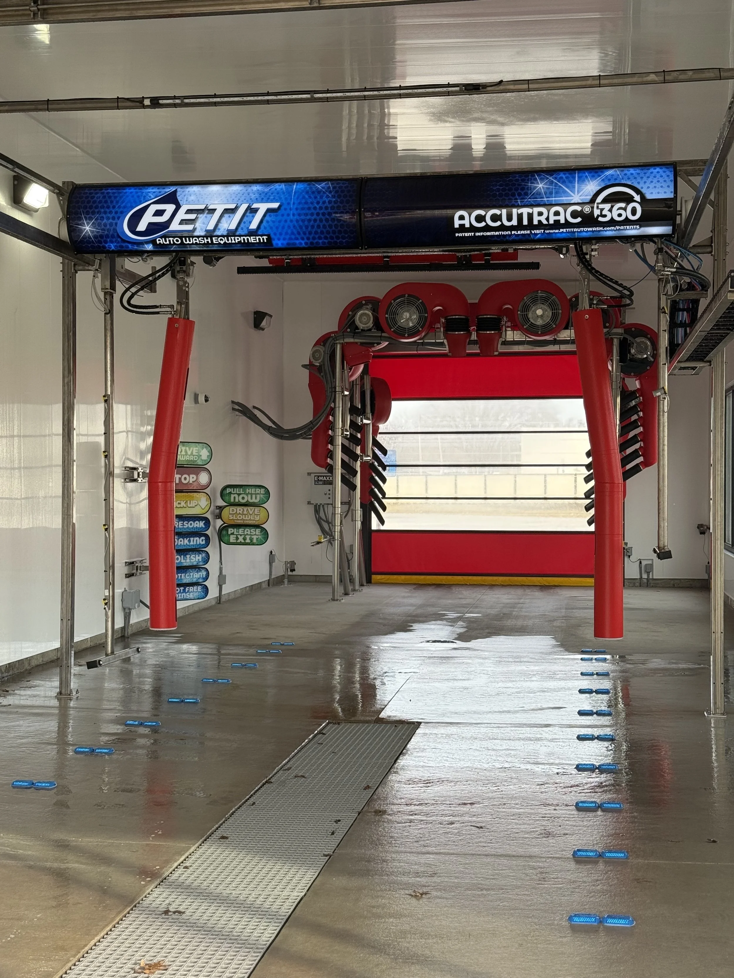 Empty car wash bay with red brushes, blue signs with instructions, and a large garage door at the back.