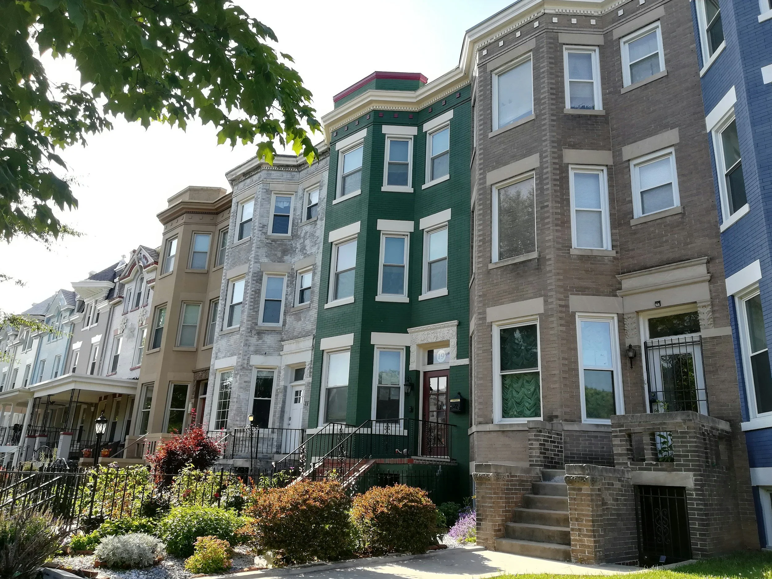 Row of colorful Victorian-style houses with front steps, windows, and garden in the foreground.