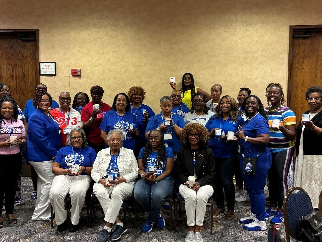 Group of women gathered indoors, some holding candles and taking photos, posing for a group picture at a conference or event.