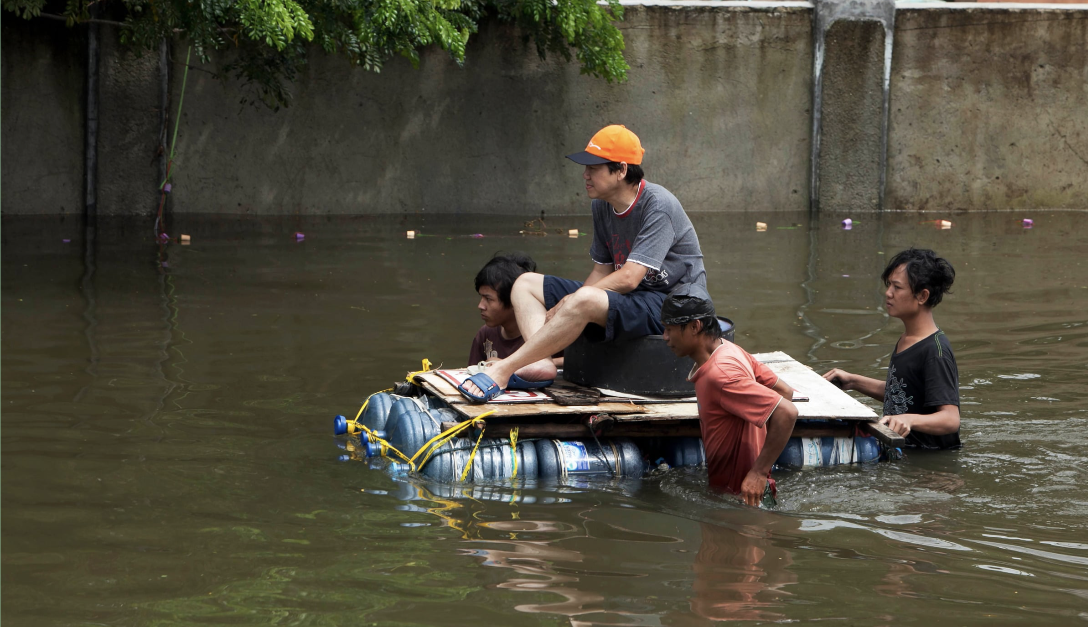 Four young men pilot a makeshift raft through flood waters