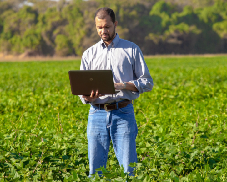 A farm manager consults his laptop PC from a field of crops