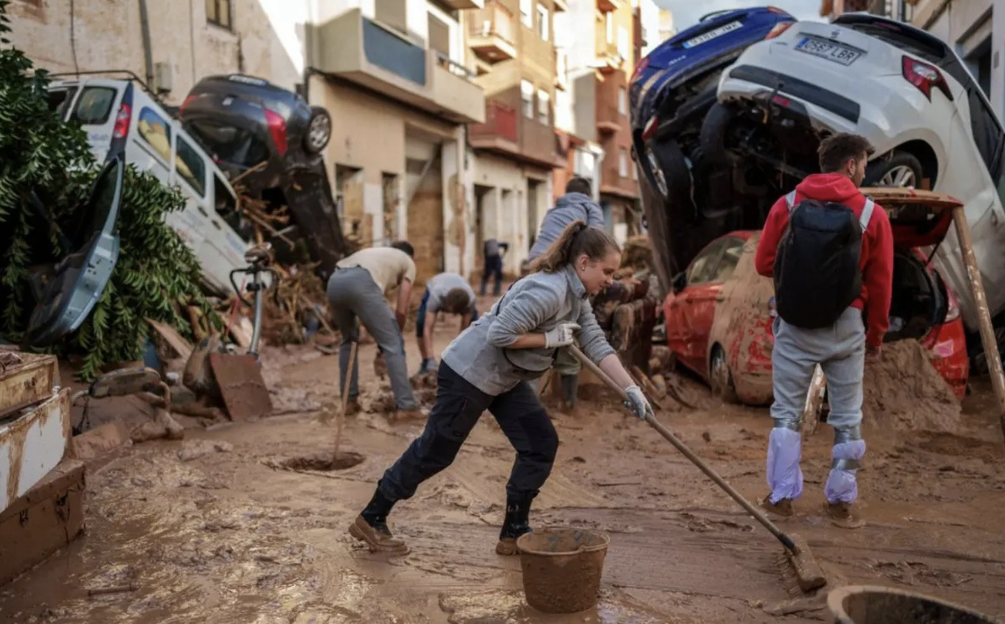 Residents perform post-flood cleanup chores amid piles of cars and debris