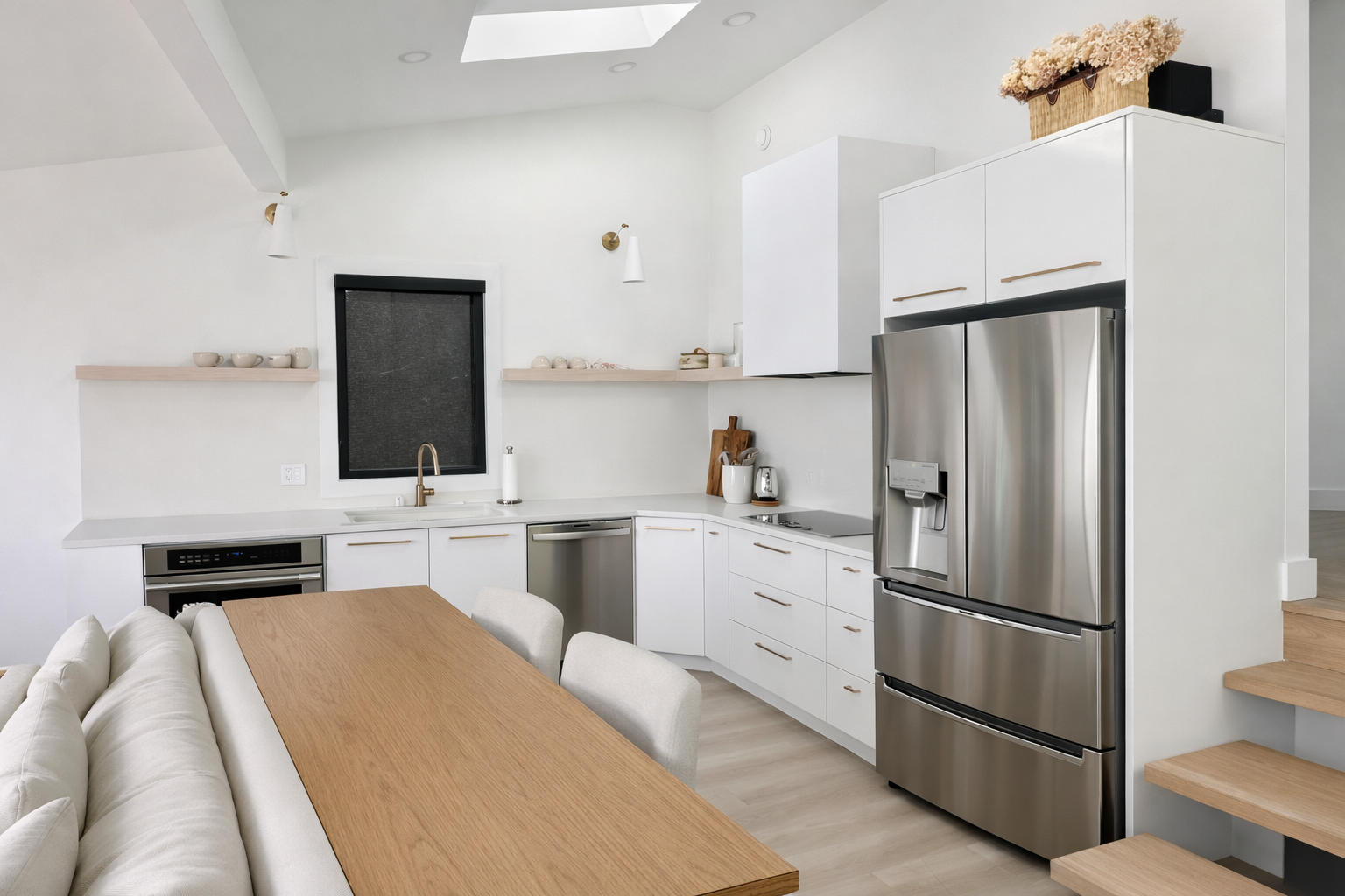 Modern kitchen with white cabinets, stainless steel refrigerator, black window, and a wooden dining table with cream chairs.