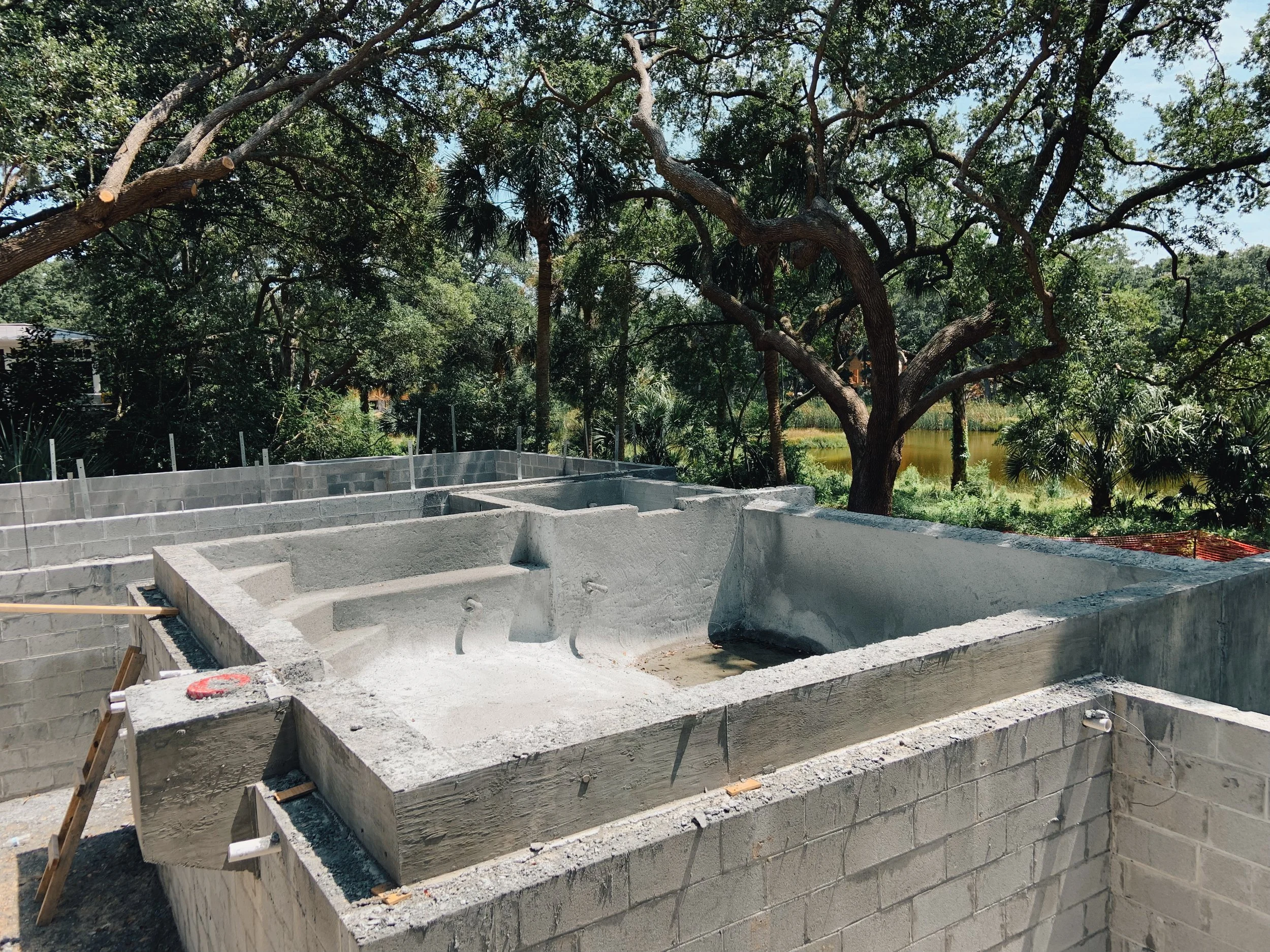 Construction site with a concrete pool or spa under construction, surrounded by trees and greenery.