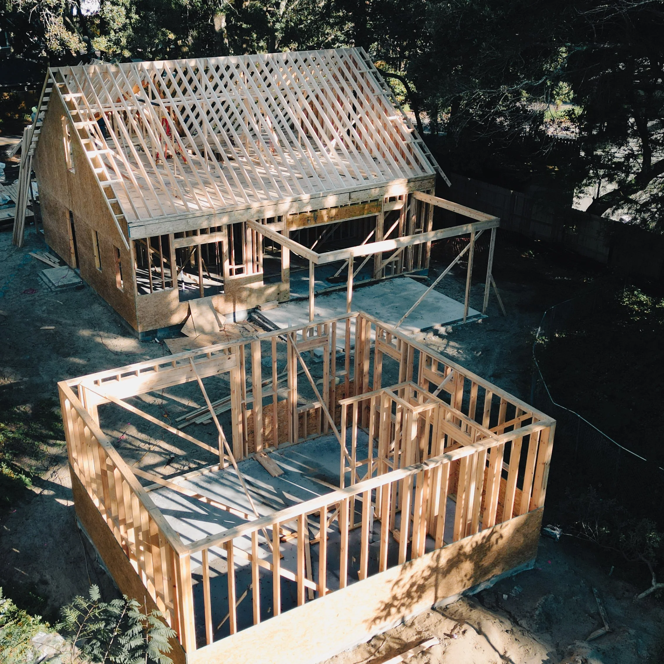 Aerial view of a house under construction with wooden framing and roof trusses in progress.