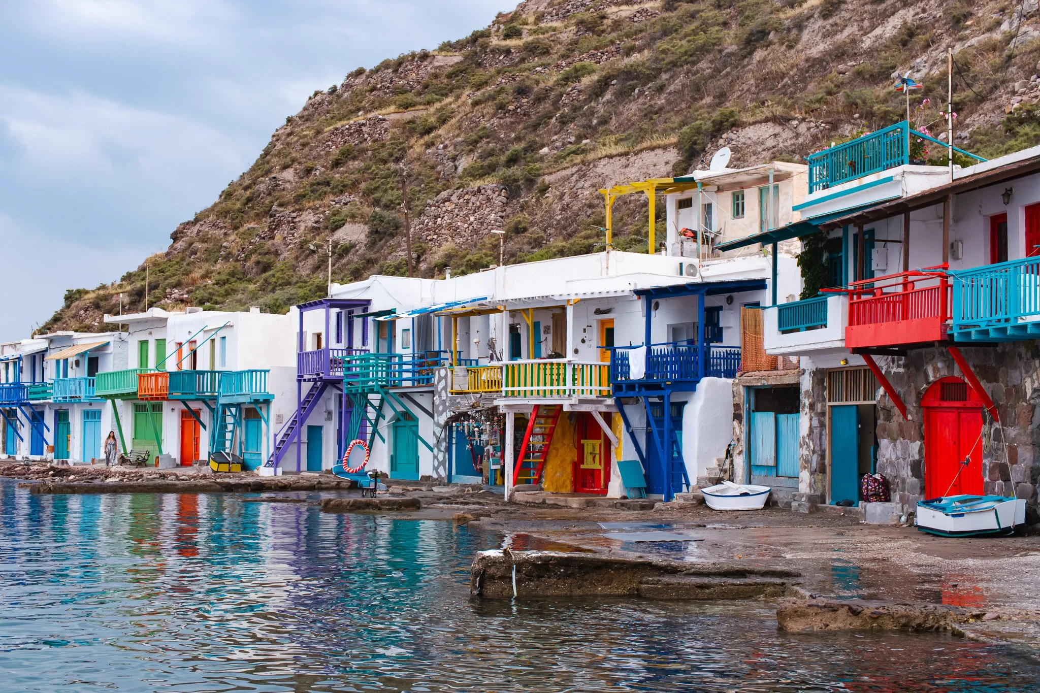 Colorful houses with balconies and boats along a waterfront with a mountainous hillside in the background