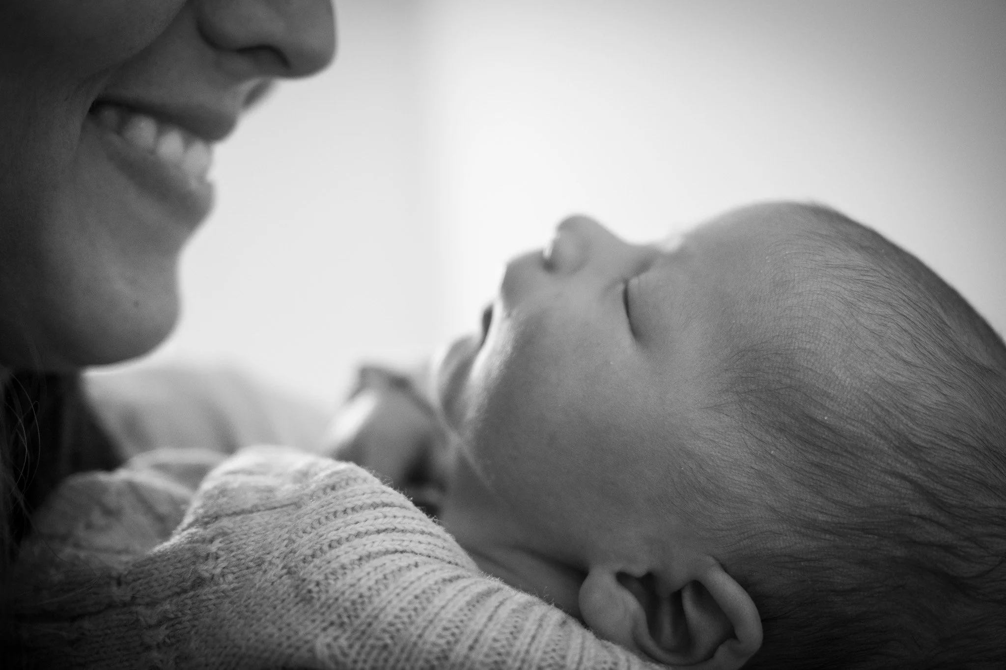 A black and white close-up of a woman smiling at a sleeping baby she is holding.