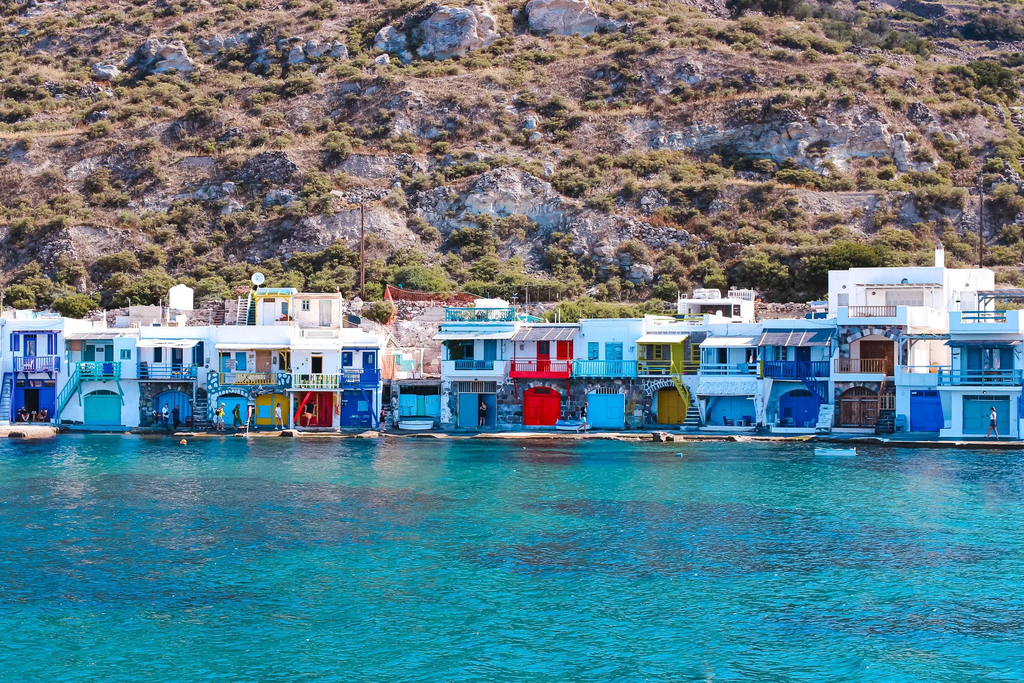 Colorful buildings along the seaside in Klima, Milos, with a rocky hillside in the background