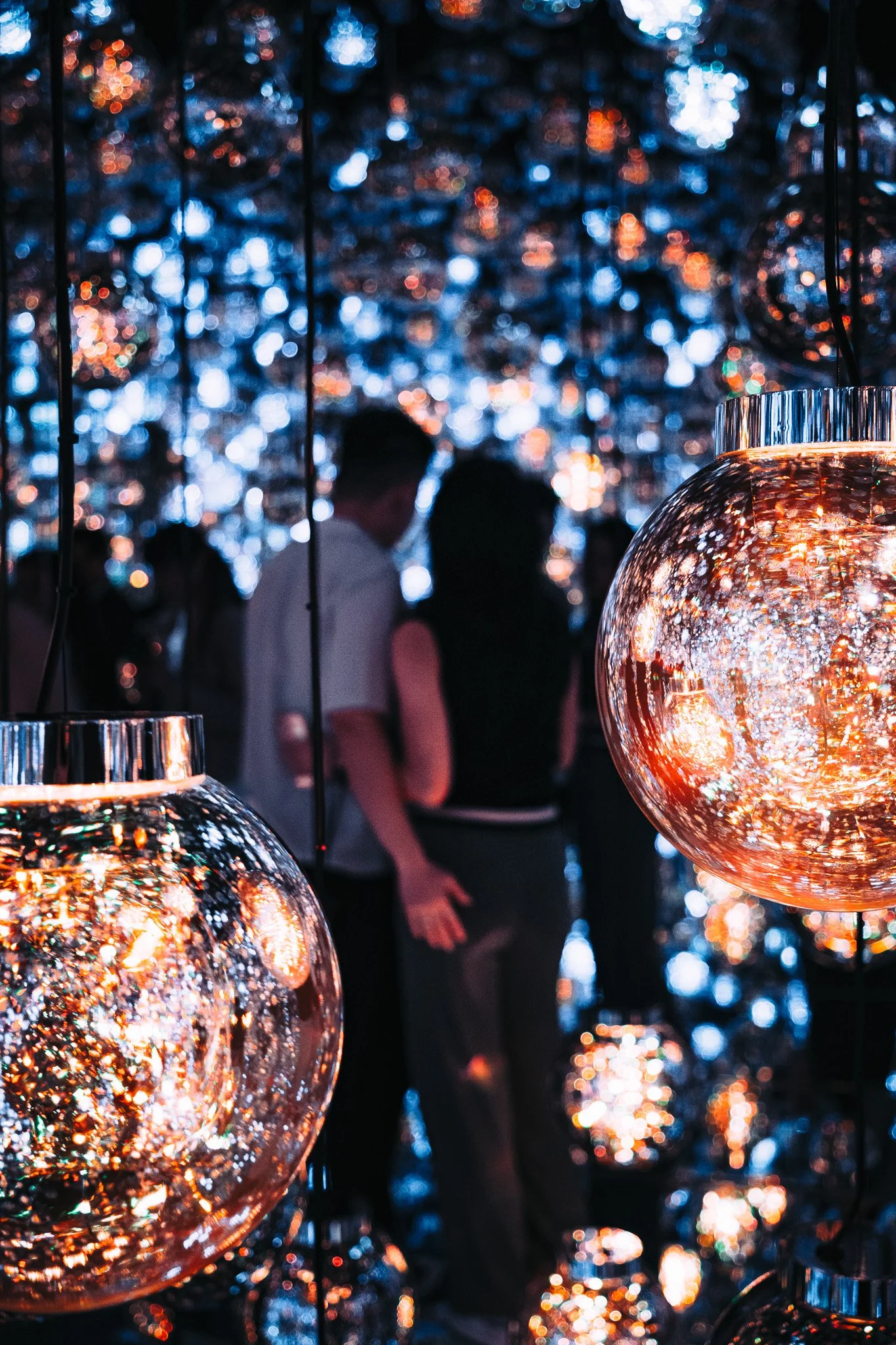A couple at Teamlabs Borderless installation with glowing, reflective hanging glass orbs.