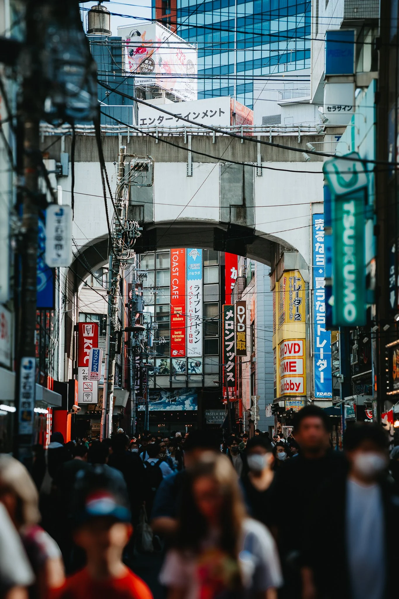 A busy street scene in Akihabara, Tokyo, Japan with many colorful signs and advertisements, and a crowd of people walking under an archway.