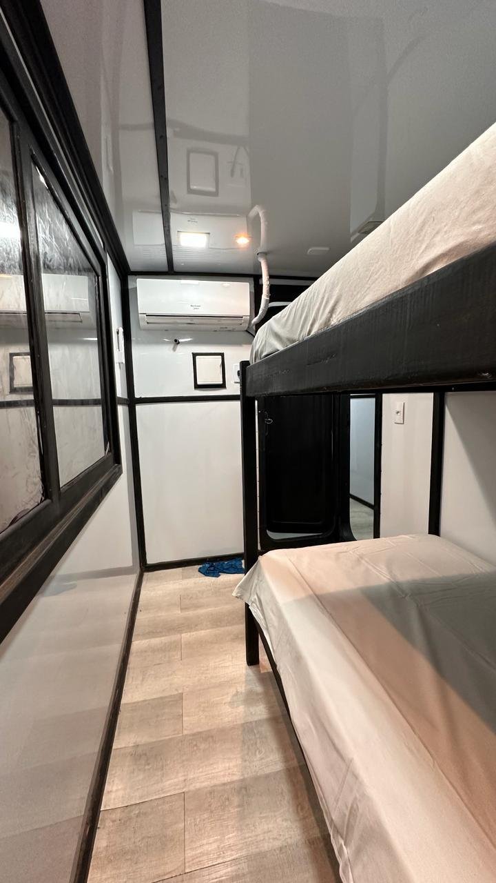 Bunk beds with white bedding in a small room with a black metal frame, a window on the left, and an air conditioning unit on the wall.