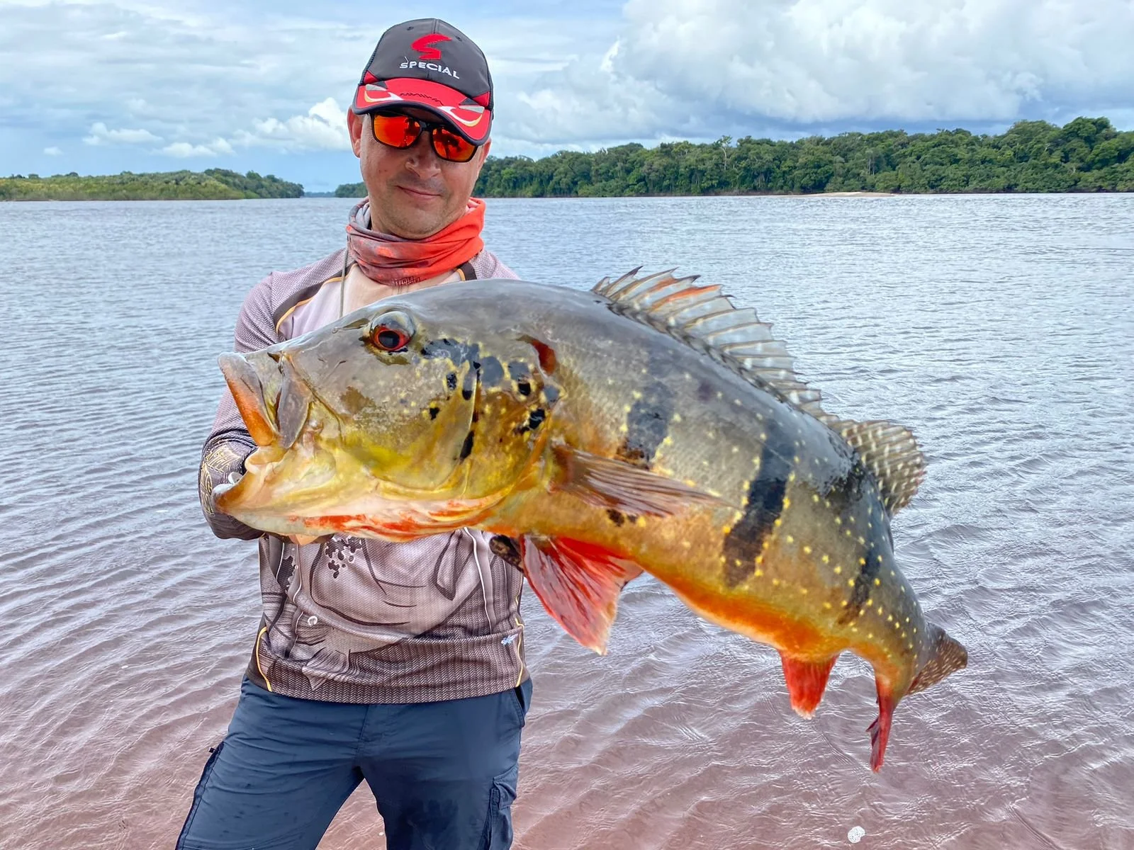 Man holding large fish on river with forested shoreline in background