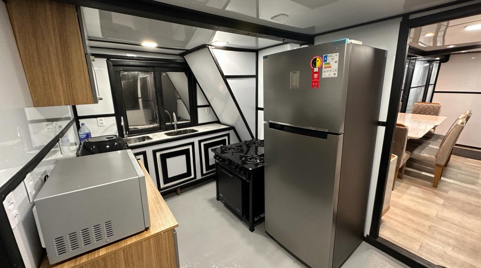 Modern kitchen with granite countertops, stainless steel refrigerator, microwave, black stove, double sink, and dining area with chairs and table.