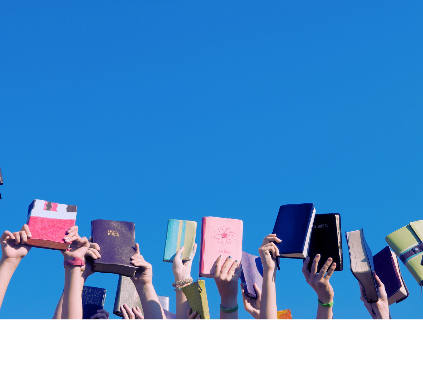 Multiple people holding up religious books and Bibles against a clear blue sky.