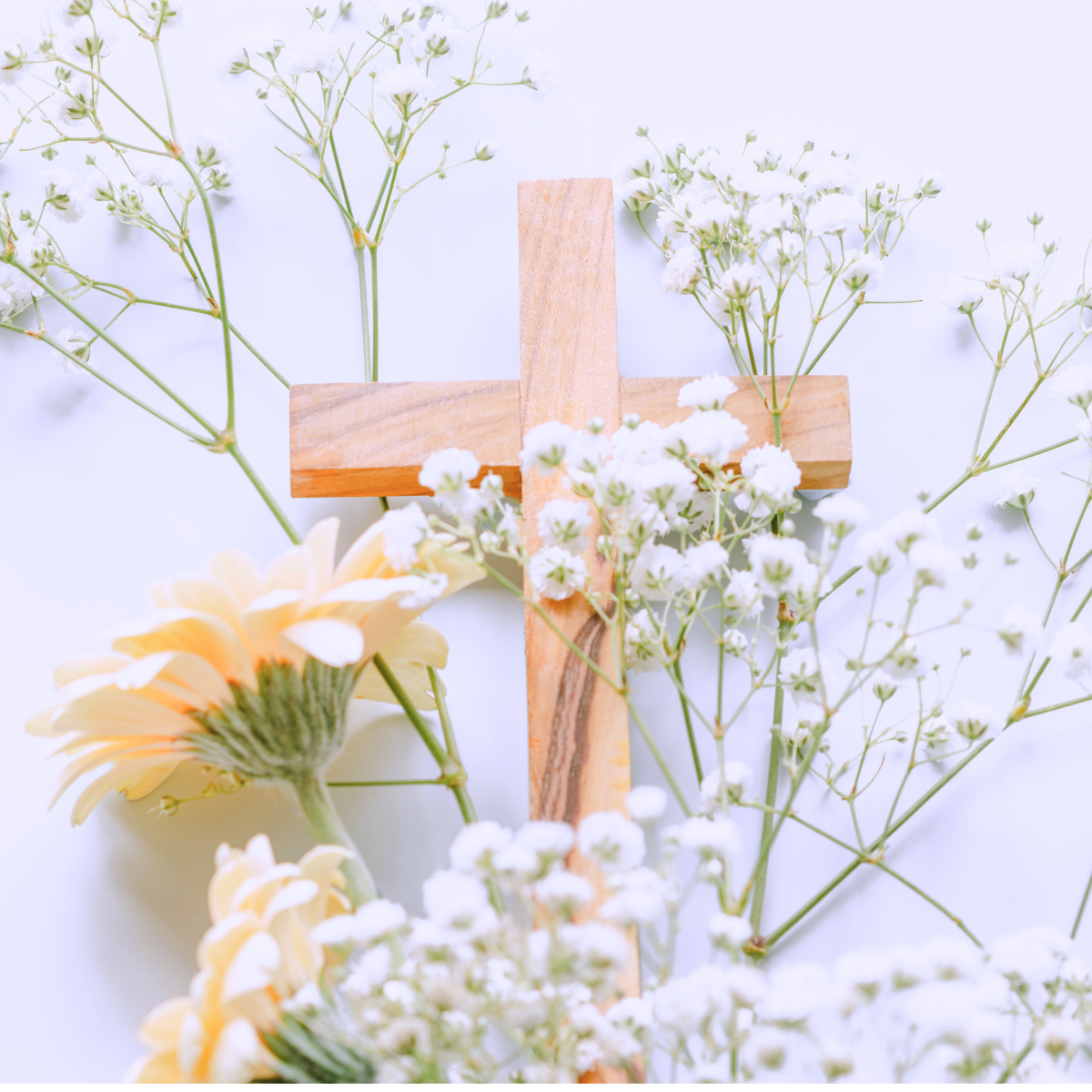 A wooden cross surrounded by white and yellow flowers on a white background.