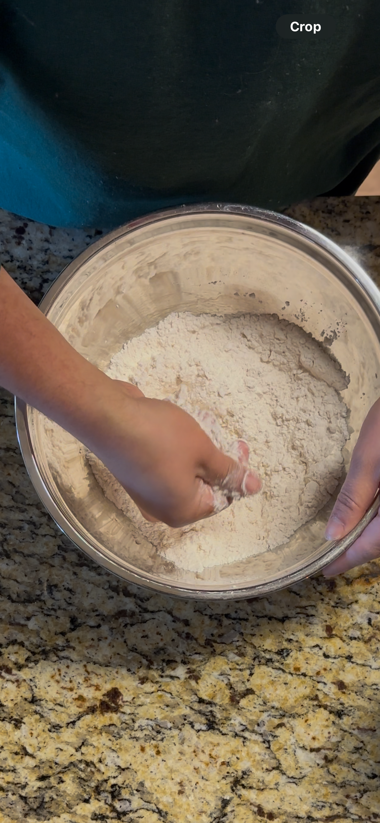 Person mixing flour in a stainless steel bowl on a granite countertop.